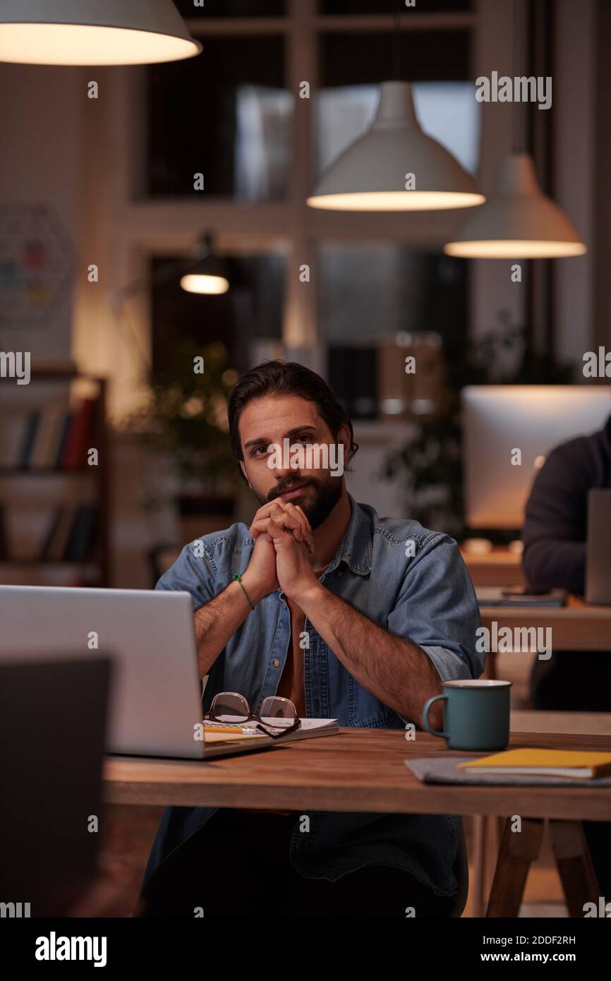 Portrait d'un jeune designer dans des vêtements décontractés assis à son lieu de travail devant l'ordinateur portable et vue sur l'appareil photo Banque D'Images