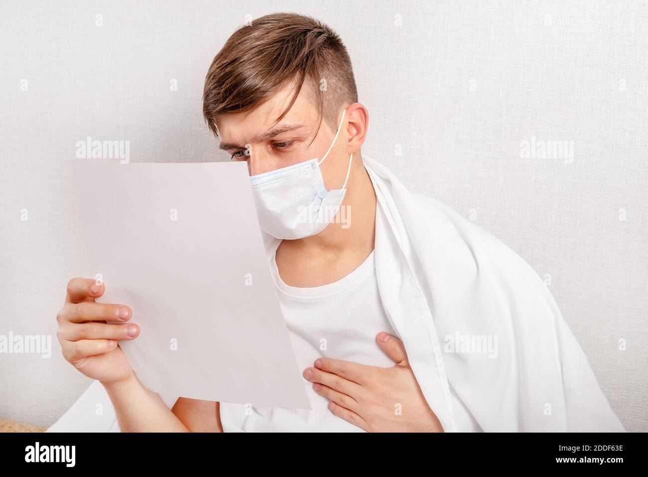 Un jeune homme inquiet dans le masque de grippe a lu un document sur Le canapé à la maison Banque D'Images