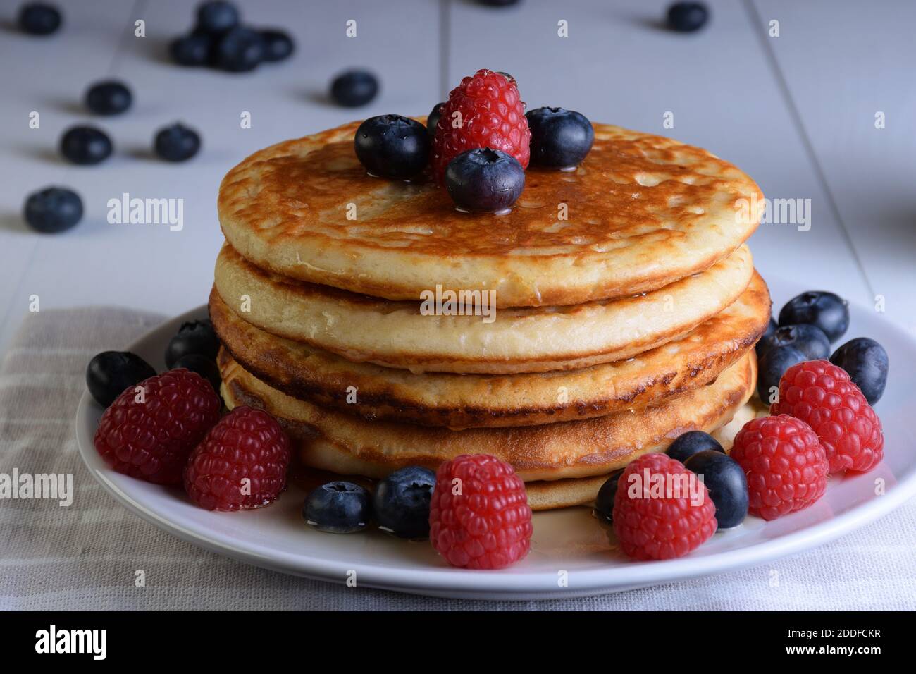 Assiette de crêpes au sirop d'érable, bleuets et framboises sur table en bois blanc. Banque D'Images