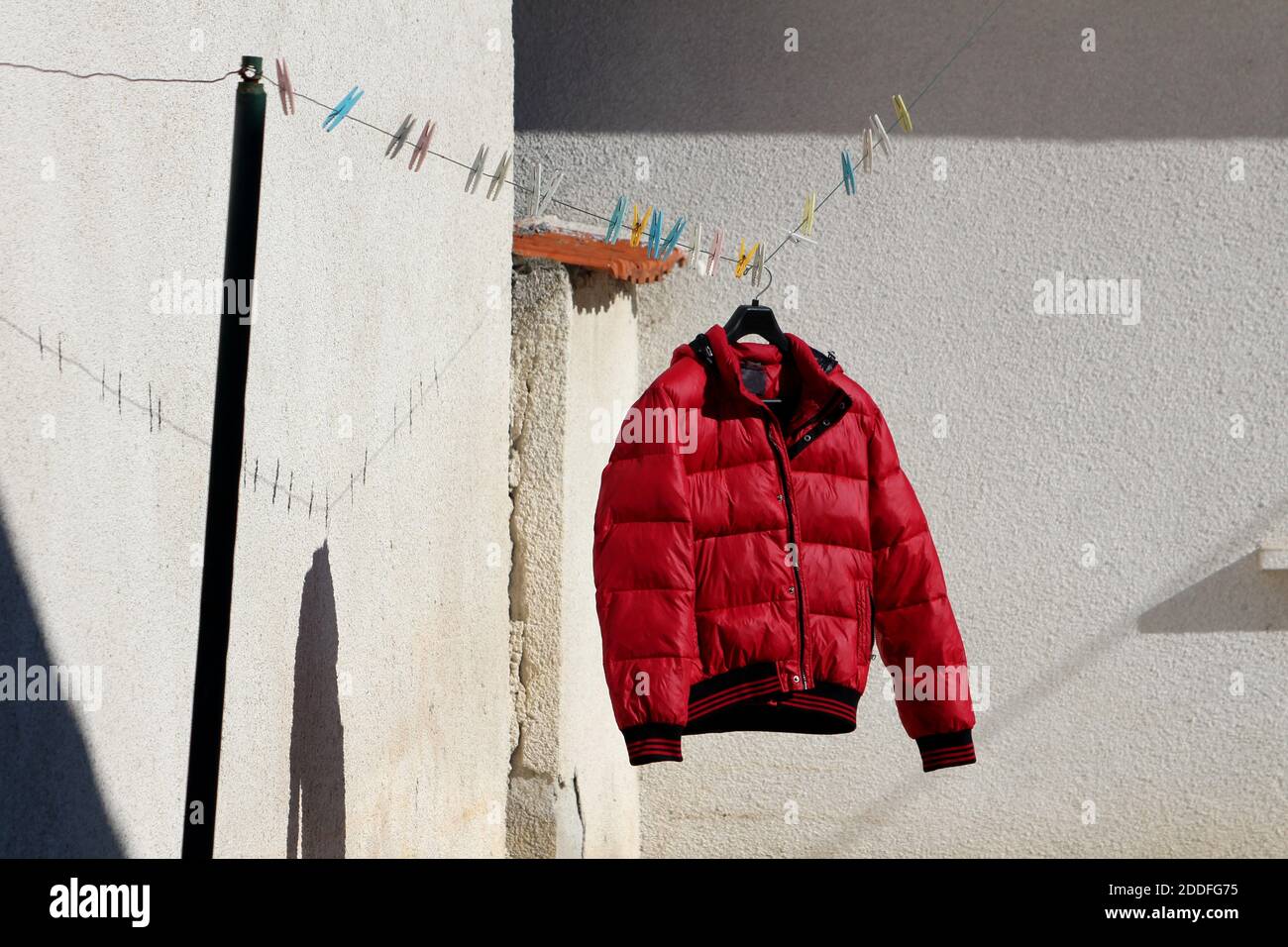 Veste d'hiver rouge vif fraîchement lavée pour sécher cintre attaché à la corde à linge remplie de cloespins dans divers couleurs dans la maison familiale Banque D'Images