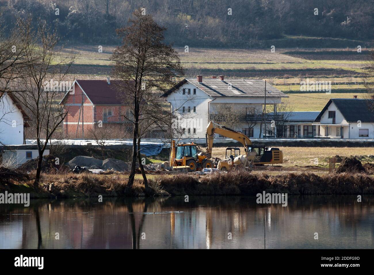 Chargeuse-pelleteuse industrielle à côté d'une pelle compacte et d'une petite chargeuse industrielle batteur sur le site local de construction du levee, à côté de la rivière calme Banque D'Images