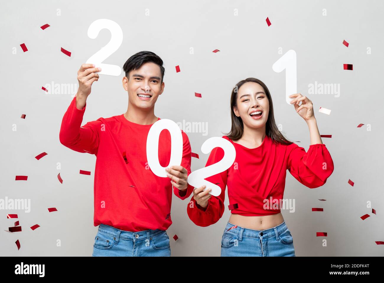 Sourire heureux asiatique couple en rouge décontracté tenue 2021 chiffres pour le nouveau concept de l'année sur fond gris clair avec confettis Banque D'Images