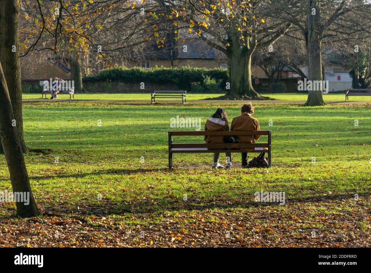 Jeune couple assis sur un banc de parc bénéficiant du soleil d'hiver, Abington Park, Northampton, Royaume-Uni Banque D'Images