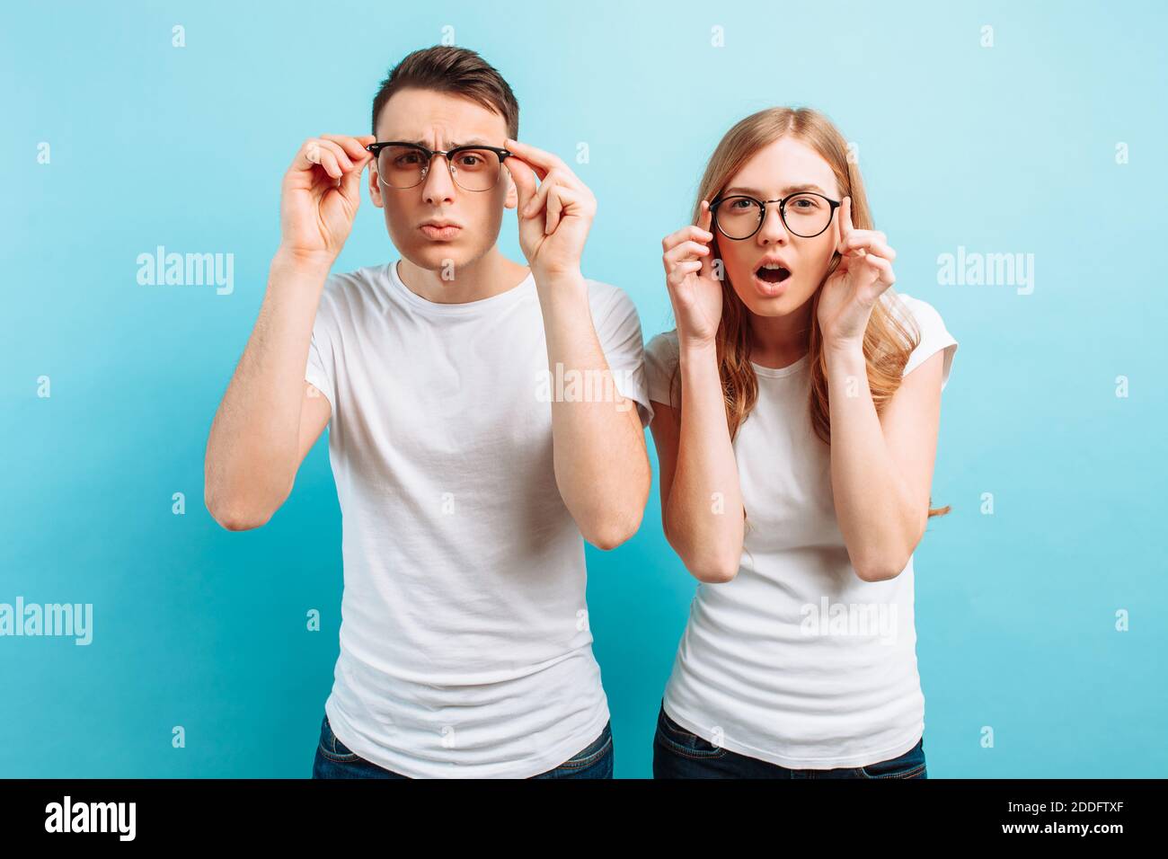 Un jeune couple avec une mauvaise vue, un homme et une femme avec des lunettes regardent dans la caméra, essayant de voir quelque chose, sur un fond bleu Banque D'Images