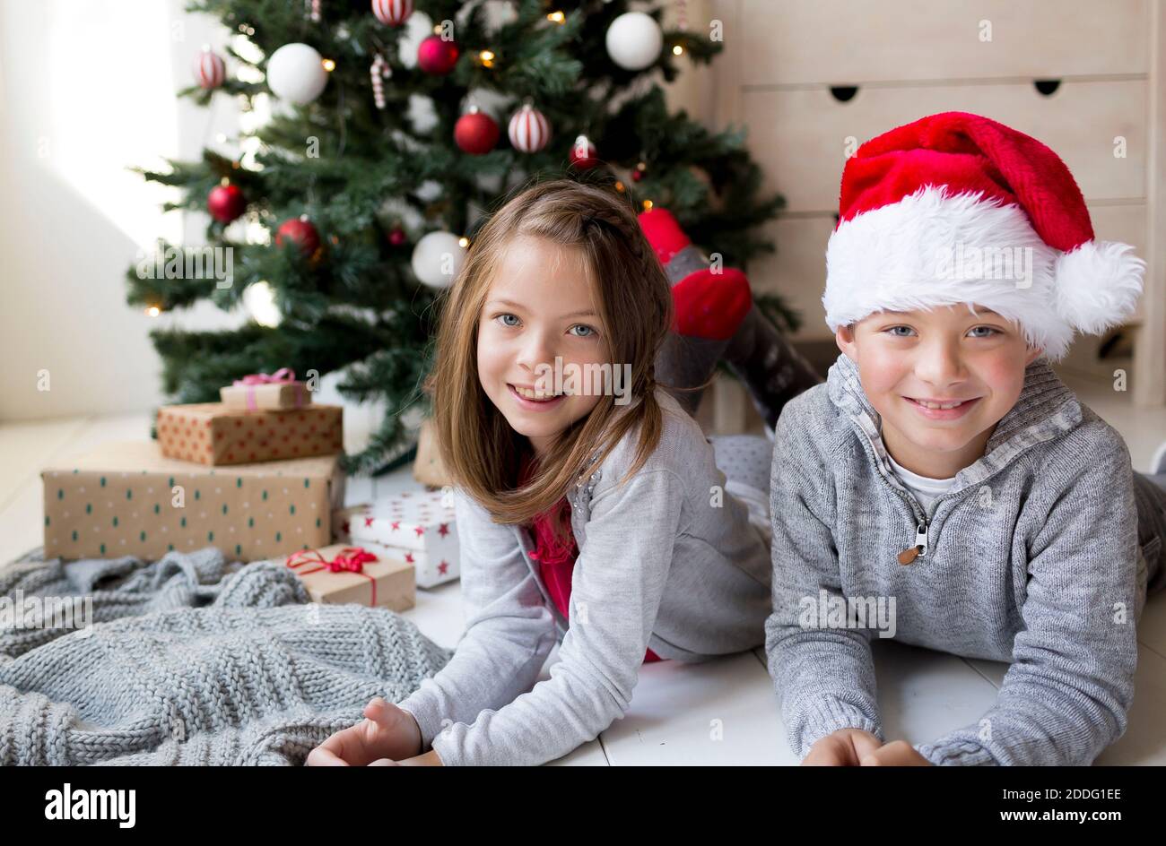 Jolie fille et garçon couché devant un Noël Arbre célébrant Noël Banque D'Images