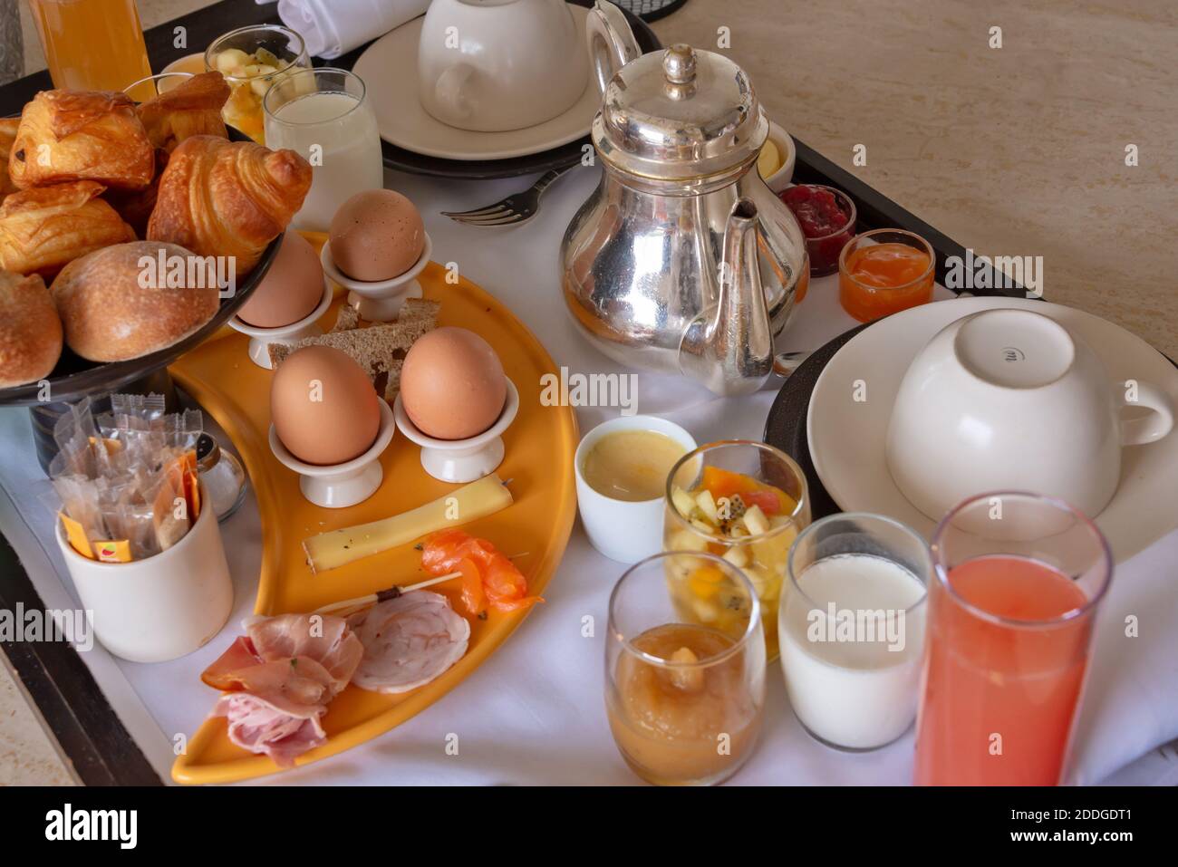 Petit déjeuner de luxe avec œufs, jambon, fruits, croissants et thé sur un plateau Banque D'Images