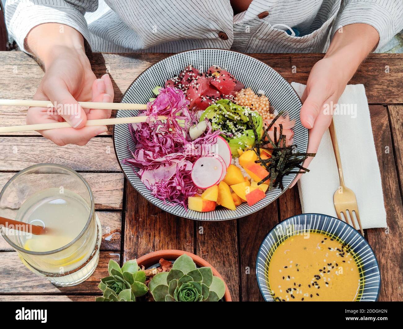 Femme mangeant savoureux coloré sain naturel bio végétarien poke bol hawaïen utilisant des baguettes asiatiques sur table rustique en bois. Naturel sain Banque D'Images