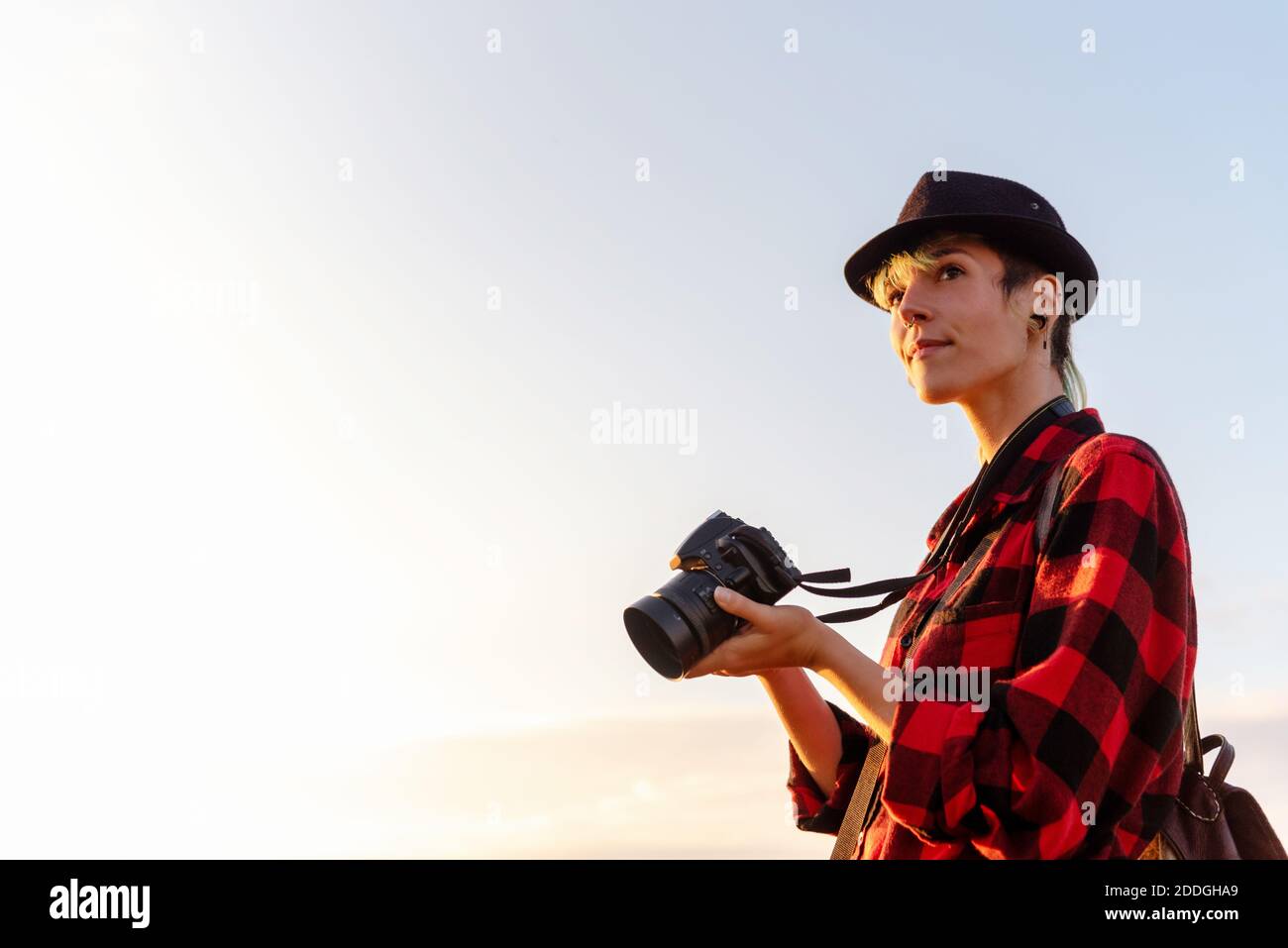 Vue latérale d'une femme voyageur androgyne avec appareil photo professionnel debout sur une colline dans une zone montagneuse Banque D'Images