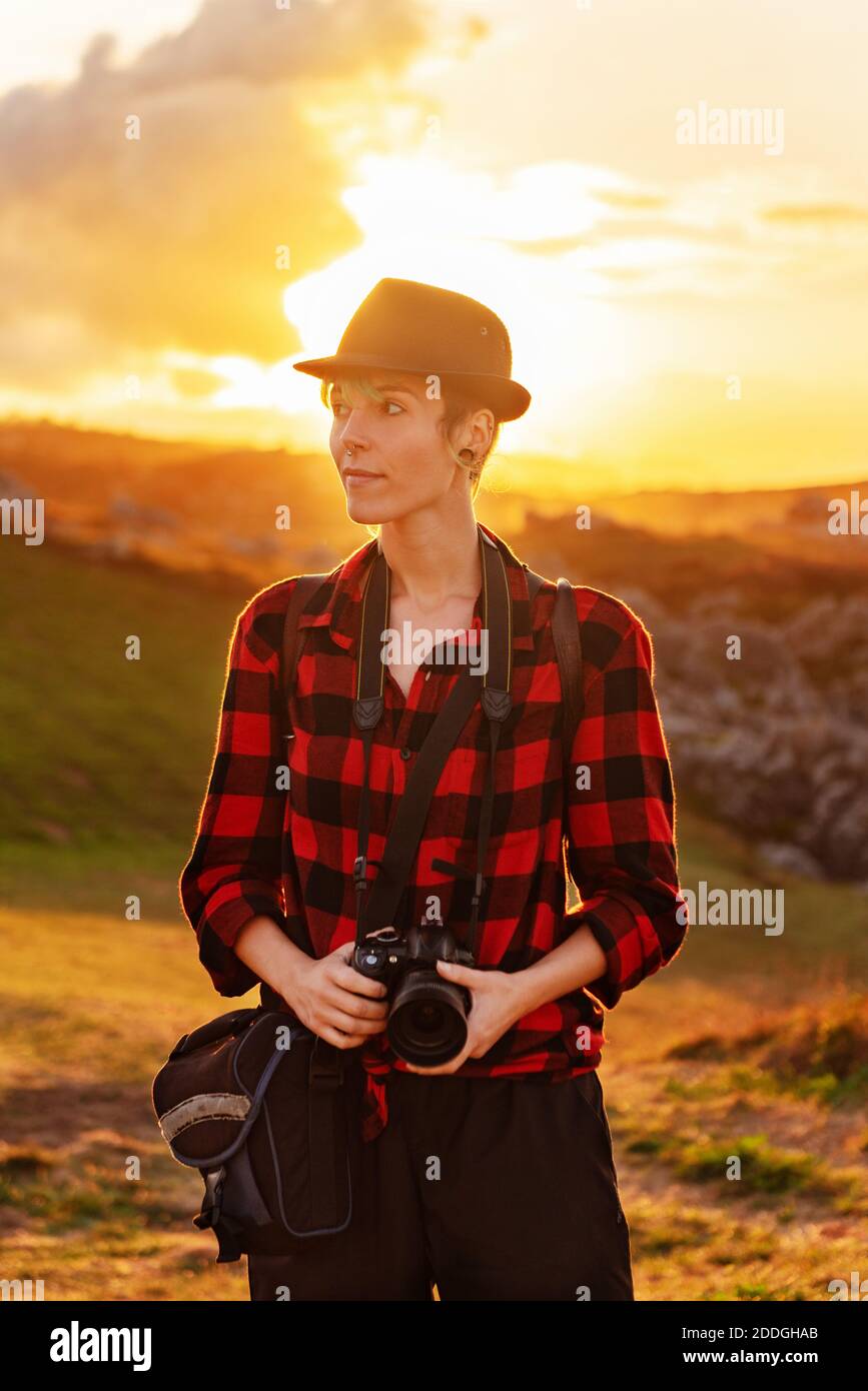 Vue de face d'une femme voyageur androgyne avec appareil photo professionnel debout sur une colline dans une zone montagneuse Banque D'Images