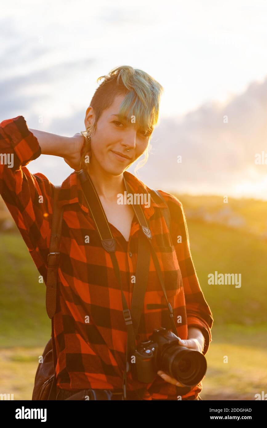 Vue latérale d'une femme voyageur androgyne avec appareil photo professionnel debout sur une colline dans une zone montagneuse Banque D'Images