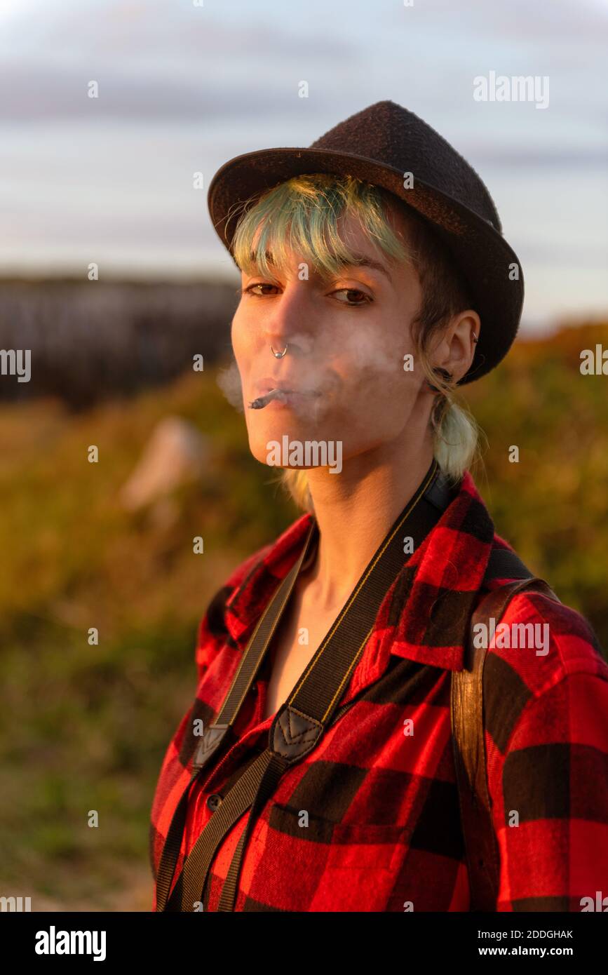 Culotte taille basse femme insouciante avec chapeau et chemise à carreaux  la nature et fumer la cigarette au coucher du soleil Photo Stock - Alamy