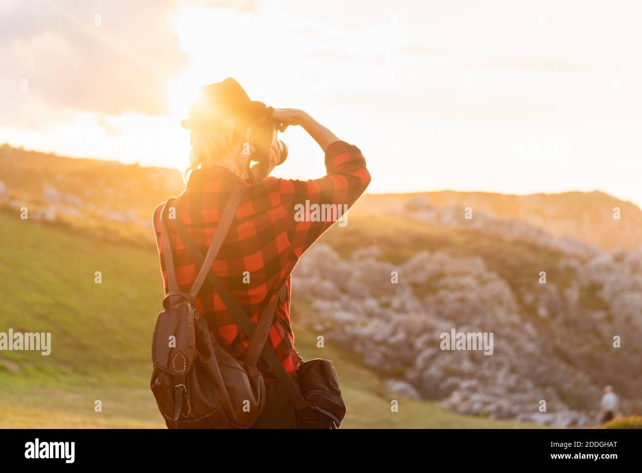 Vue arrière d'une femme voyageur androgyne avec appareil photo professionnel debout sur une colline dans une zone montagneuse Banque D'Images