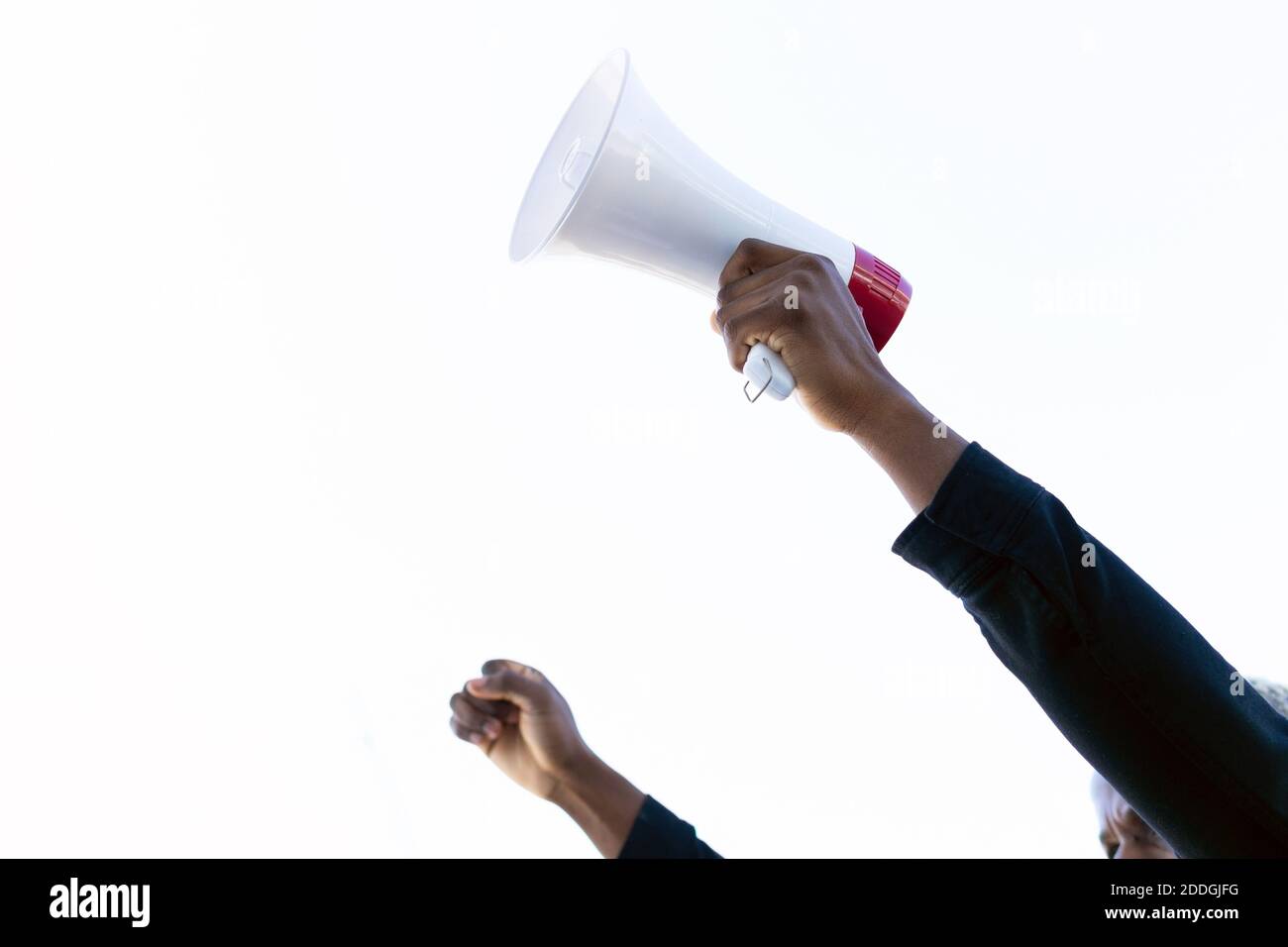 Récolte inreconnaissable de l'Afro-américain avec le mégaphone rouge et blanc debout avec le poing vers le haut sur fond blanc Banque D'Images