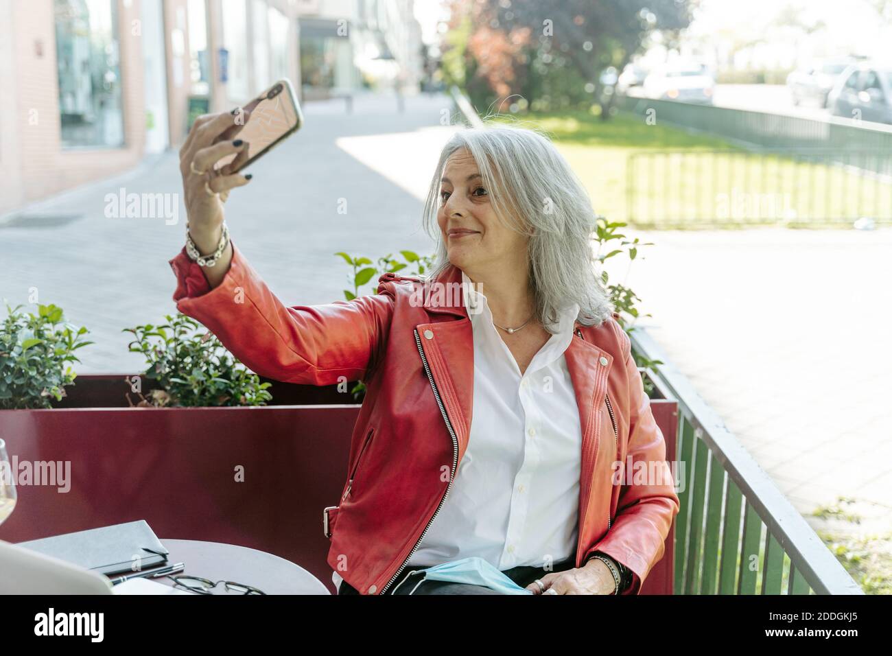 Une femme d'âge moyen ravie avec des cheveux gris qui prennent le selfie smartphone assis dans un café à l'extérieur et en attente de la commande Banque D'Images