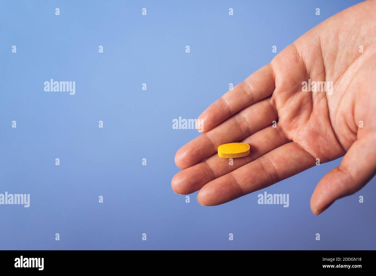 Du dessus de la palmier de récolte de la personne anonyme démontrant le jaune vitamine pilule pour un style de vie sain concept contre fond bleu Banque D'Images