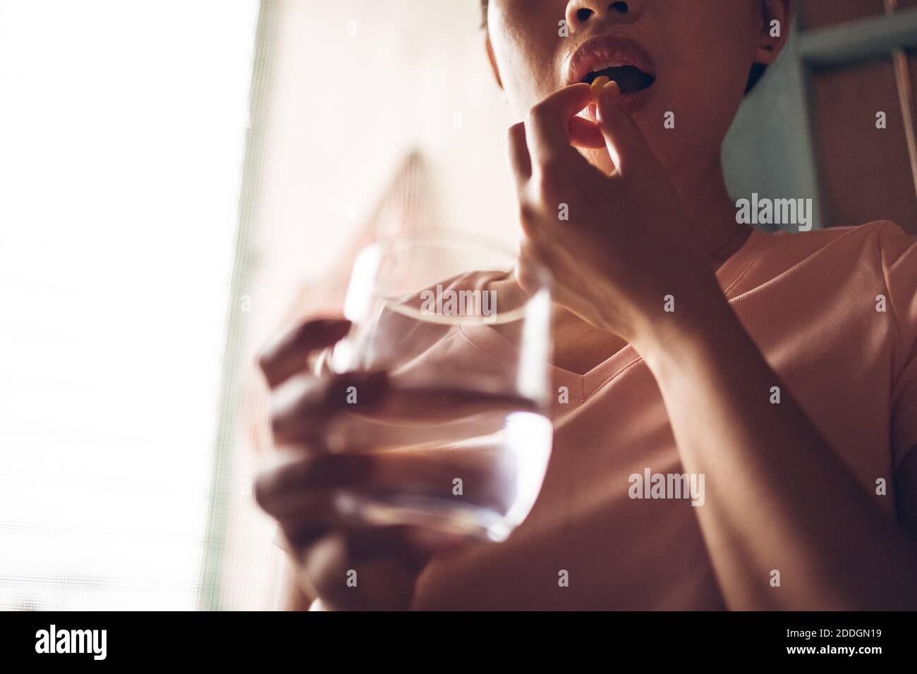 Récolte femelle méconnaissable avec un verre d'eau douce prenant jaune pilule de vitamine tout en représentant le concept de mode de vie sain Banque D'Images