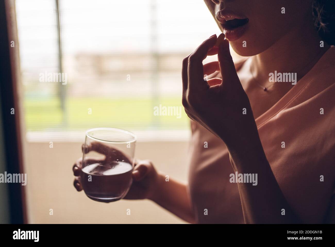 Récolte femelle méconnaissable avec un verre d'eau douce prenant jaune pilule de vitamine tout en représentant le concept de mode de vie sain Banque D'Images