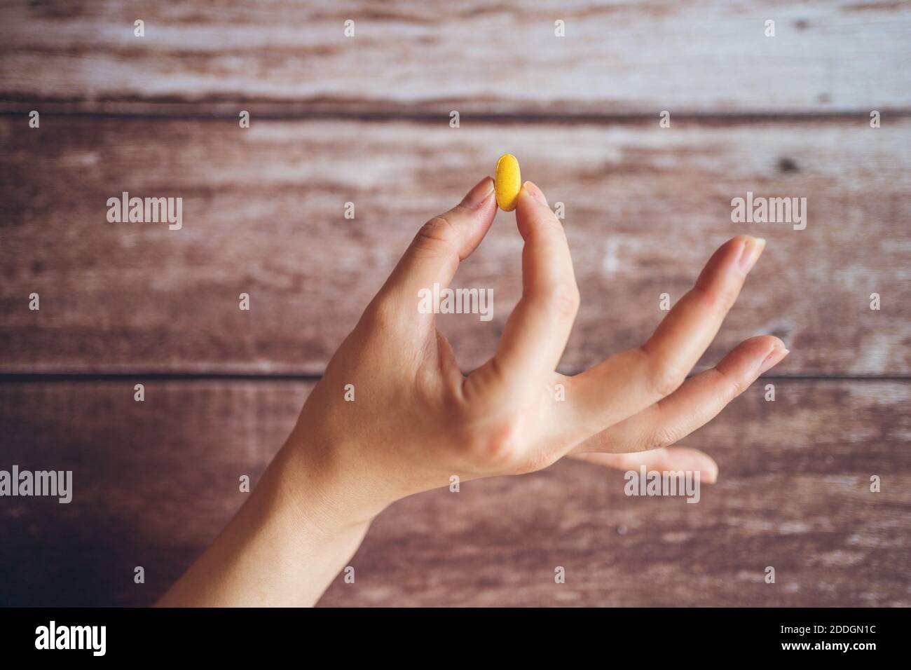 Crop main de femelle anonyme démontrant jaune vif supplément pilule pour une alimentation saine et un concept de style de vie contre un arrière-plan en bois de merde Banque D'Images