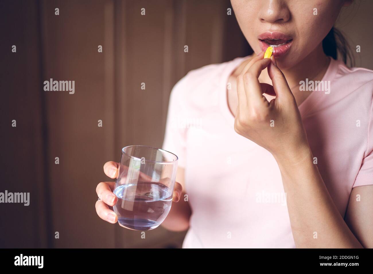 Récolte femelle méconnaissable avec un verre d'eau douce prenant jaune pilule de vitamine tout en représentant le concept de mode de vie sain Banque D'Images