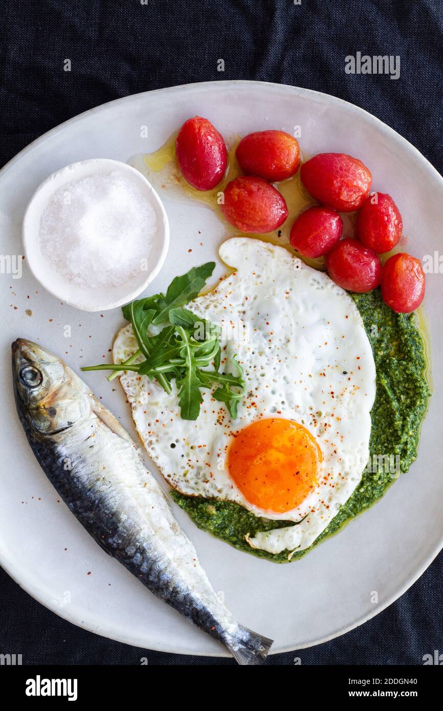 D'œufs frits au-dessus, servis avec du poisson salé et marinés tomates et garniture de sauce pesto Banque D'Images