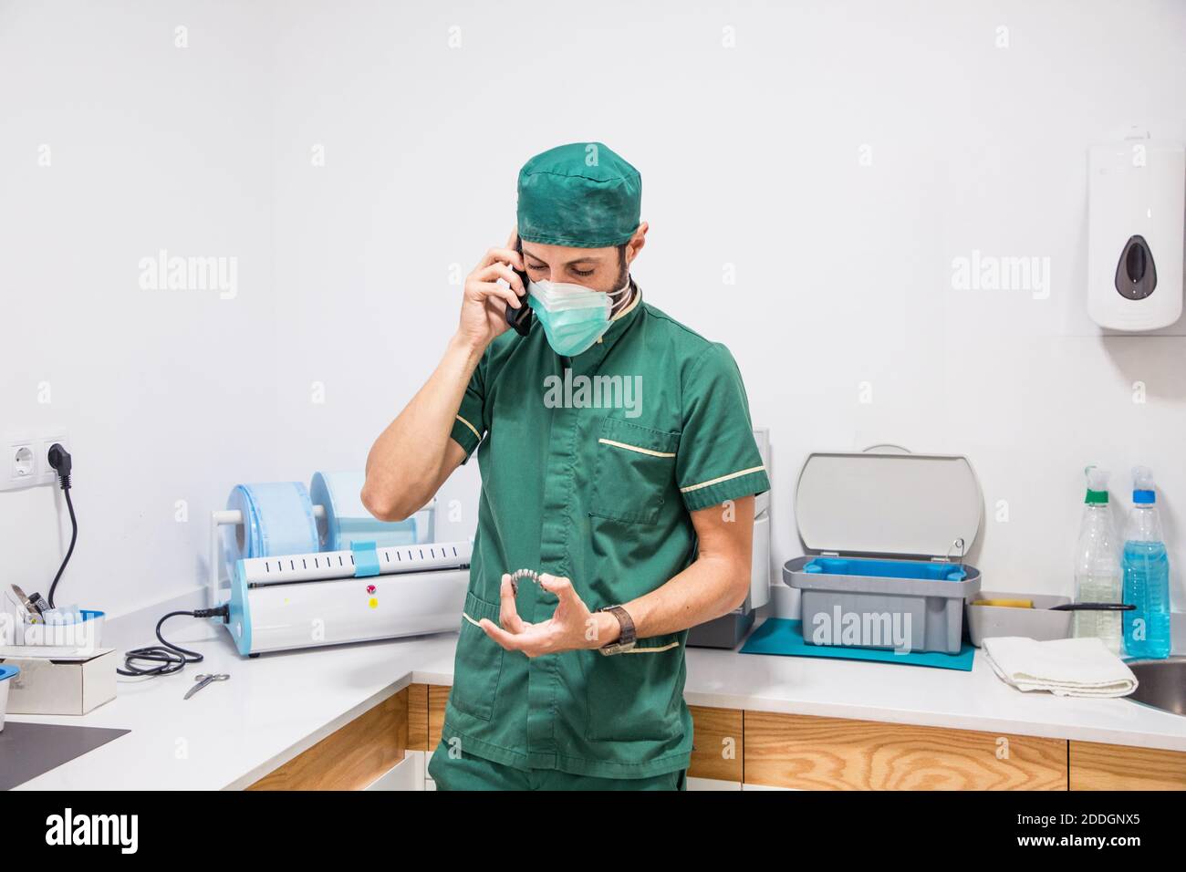 Dentiste masculin en masque et uniforme parlant sur smartphone pendant tenir le plâtre dentaire dans l'hôpital dentaire moderne Banque D'Images