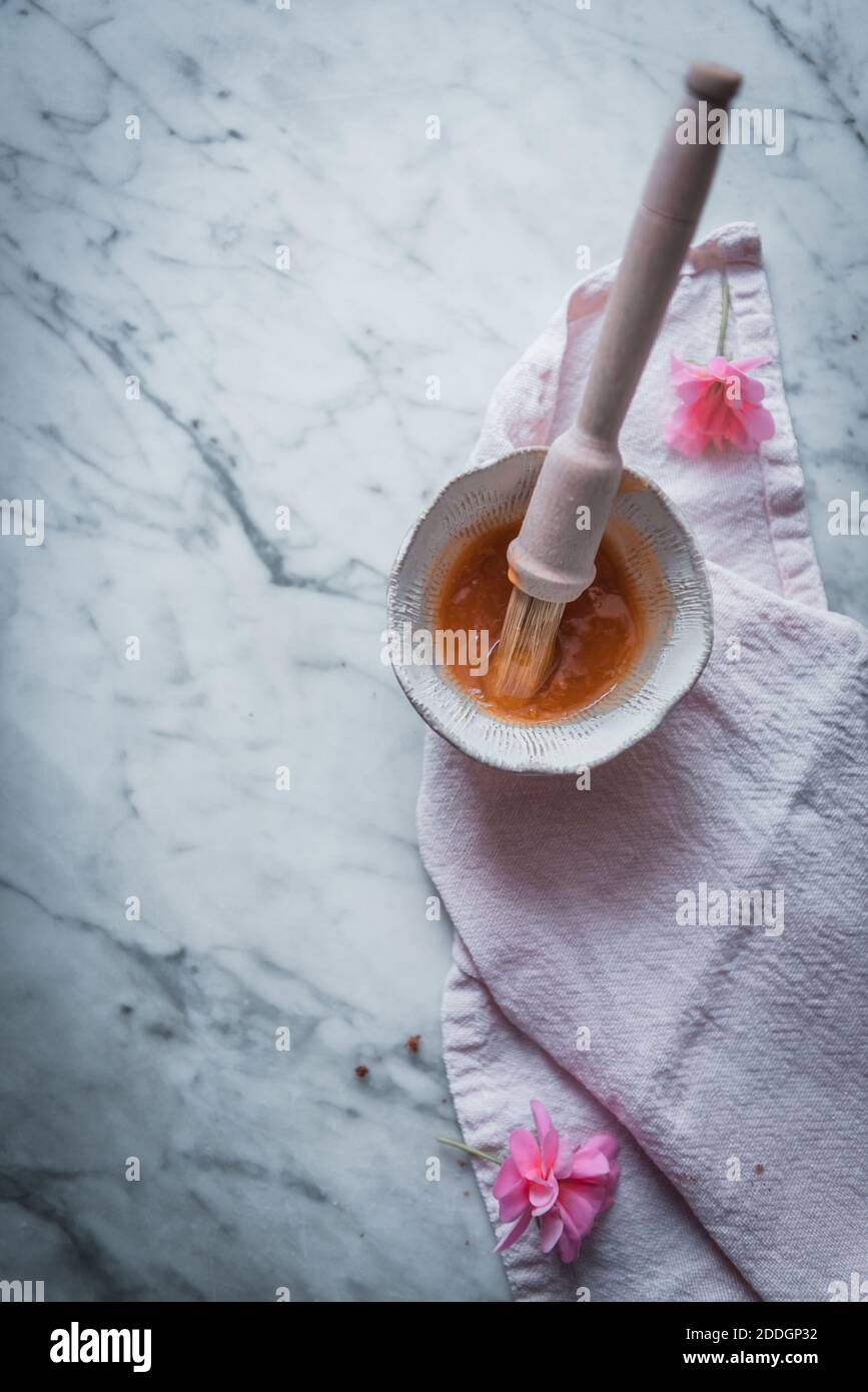 Vue de dessus du bol avec sirop sucré et brosse de cuisine préparé pour l'épandage sur une pâtisserie maison placée sur une table en marbre Banque D'Images