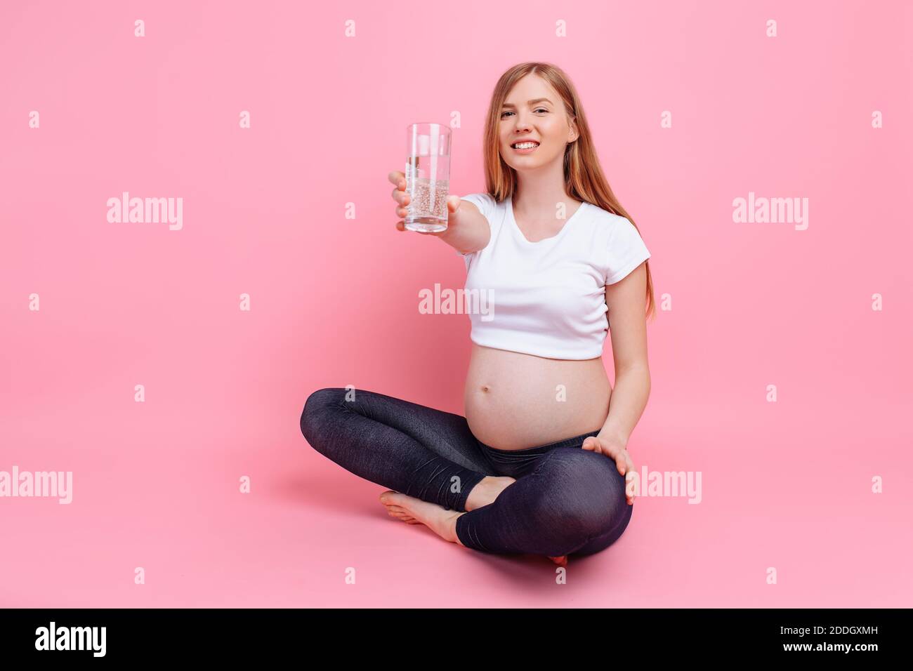 Fille enceinte tenant un verre d'eau sur le fond d'un ventre enceinte, sur un fond rose, le concept de la quantité d'eau consommée Banque D'Images