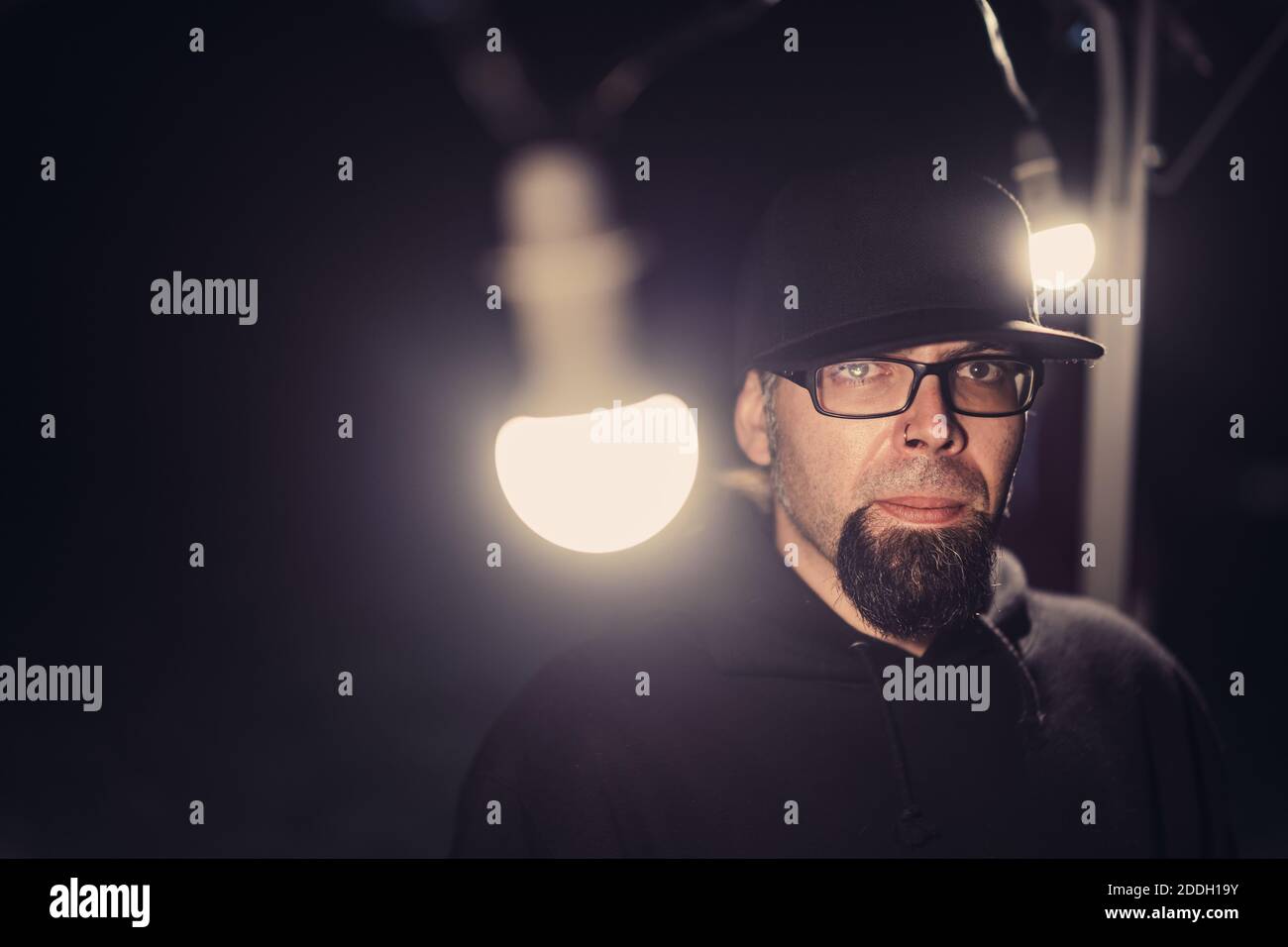 Gros plan d'un homme barbu à capuche noire lunettes et capuchon avec lumières Banque D'Images