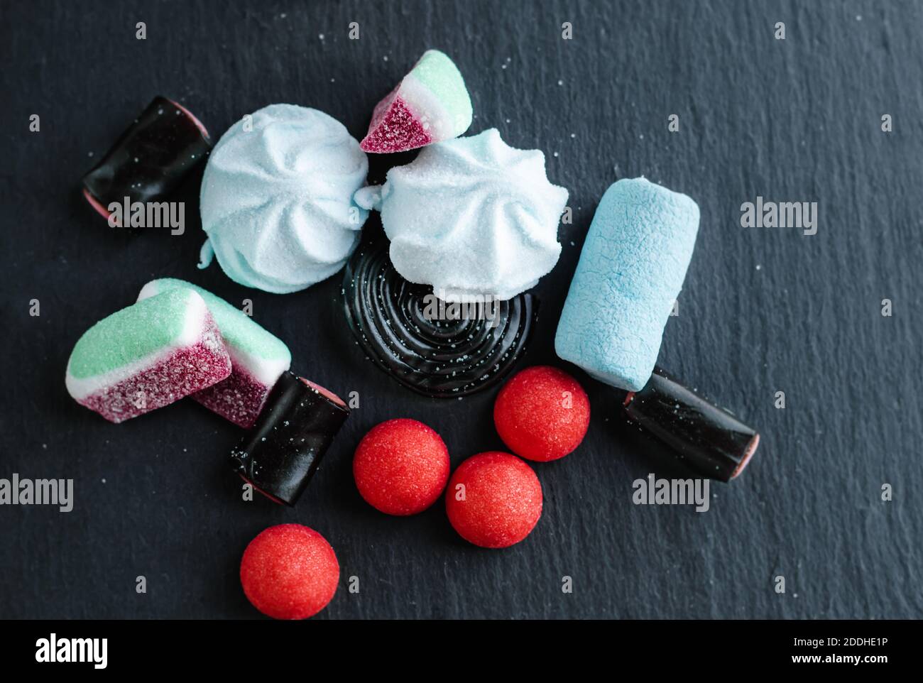Sucreries de réglisse noire, marmelade de fruits colorée dans le sucre et guimauve éparpillées en désordre sur un dessus noir rassis. Banque D'Images