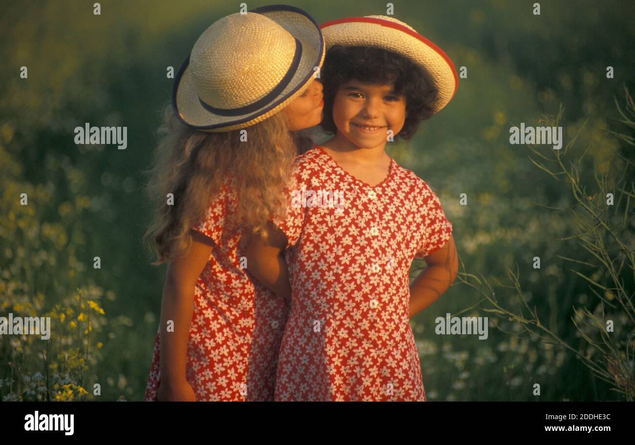 deux sœurs en chapeaux de paille debout dans un pré de pâquerettes au coucher du soleil Banque D'Images