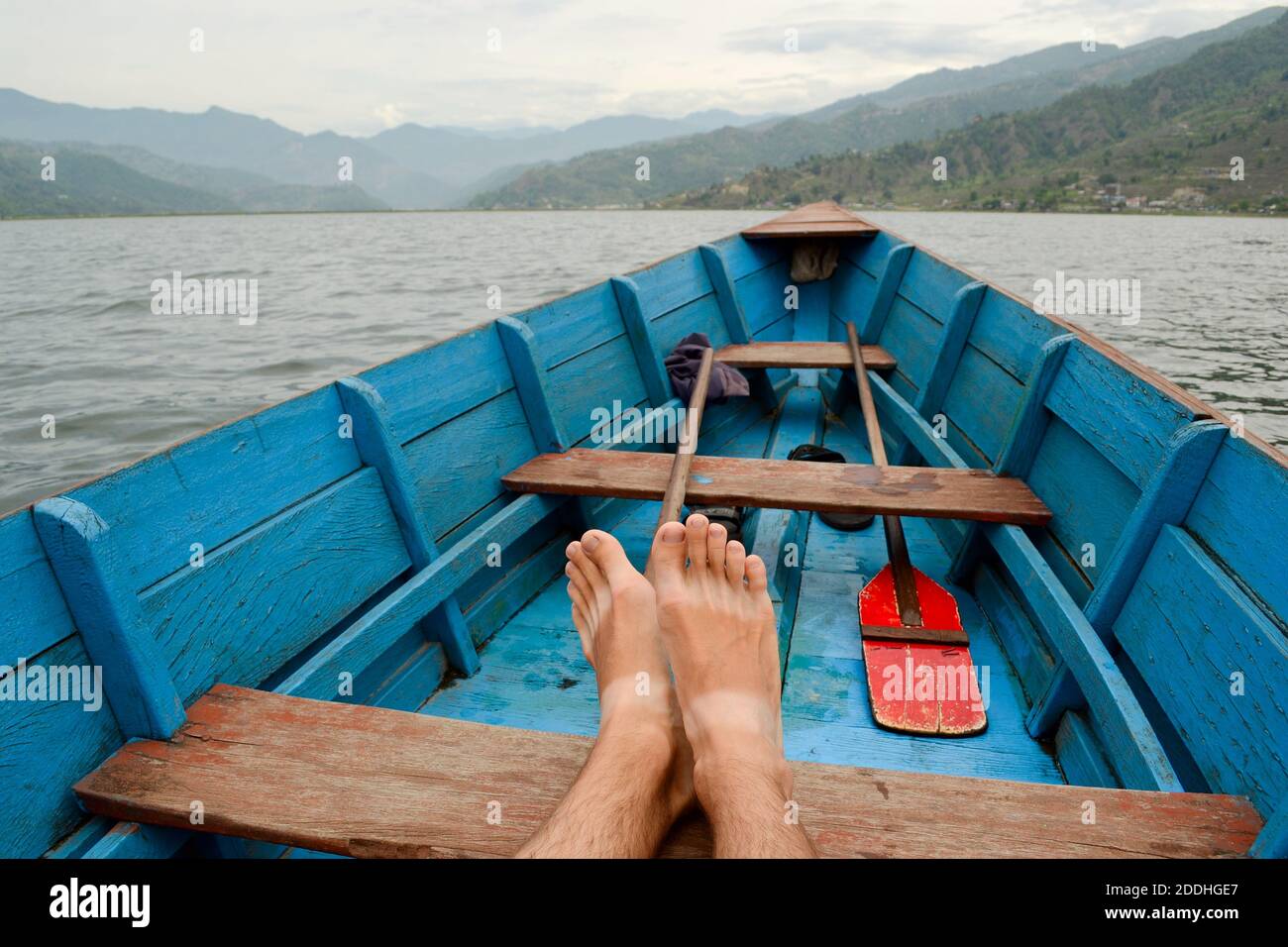 Voyageur se relaxant dans un vieux bateau en bois sur le lac Phewa à Pokhara, Népal. Vue de POV, jambes gros plan sur l'arrière-plan du paysage de montagne Banque D'Images