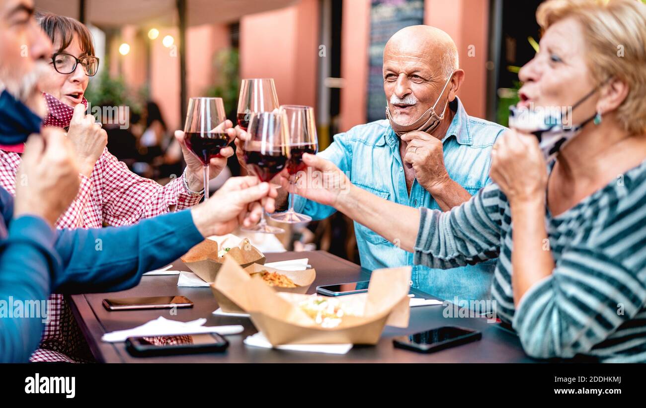 Des amis expérimentés toastent du vin au bar du restaurant en portant un visage ouvert Masque - Nouveau concept de style de vie normal avec des personnes matures heureux s'amuser ensemble Banque D'Images