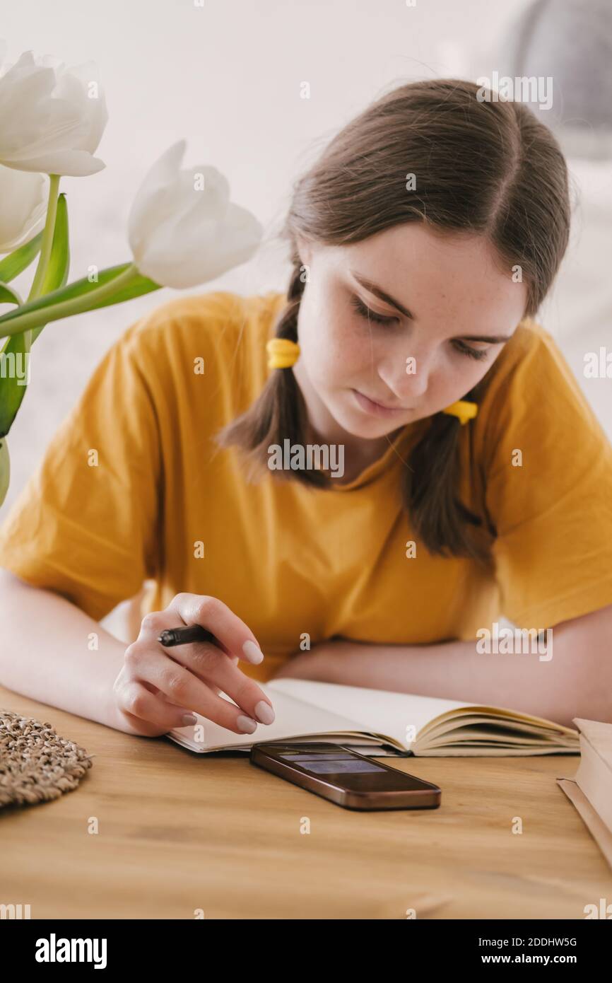 Jeune belle femme en t-shirt jaune engagé dans le travail, les affaires en ligne, étudiant assis à la table à la maison. Auto-isolement, étude, travail pendant le quaran Banque D'Images