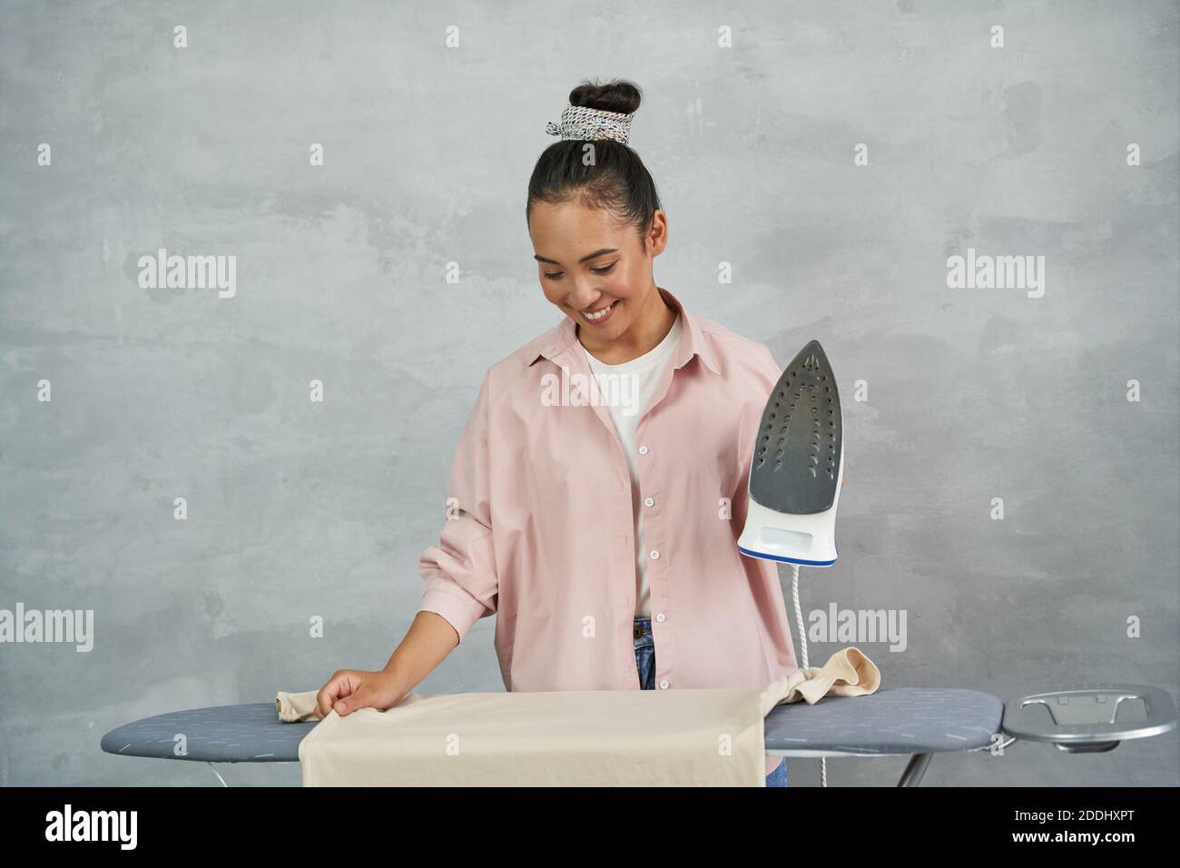 Frais et repassés. Belle jeune femme souriant tout en repassant des vêtements sur la planche à repasser à la maison. Les travaux ménagers, les tâches ménagères Banque D'Images