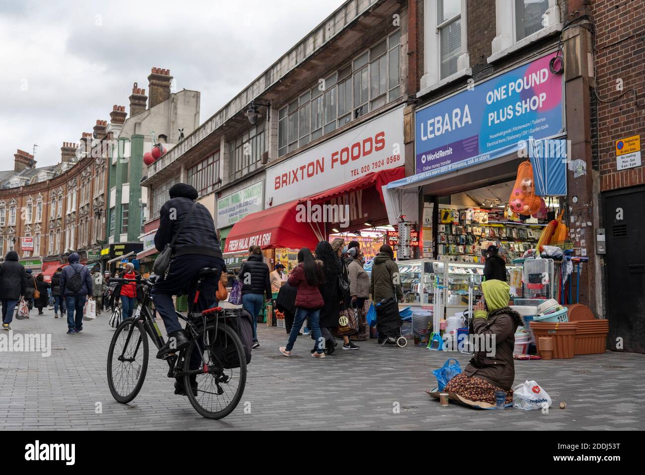 Brixton, Angleterre. Un cycliste et un mendiant de rue au marché de Brixton pendant le second confinement britannique le 21 novembre 2020 à Brixton, Londres, Angleterre Banque D'Images