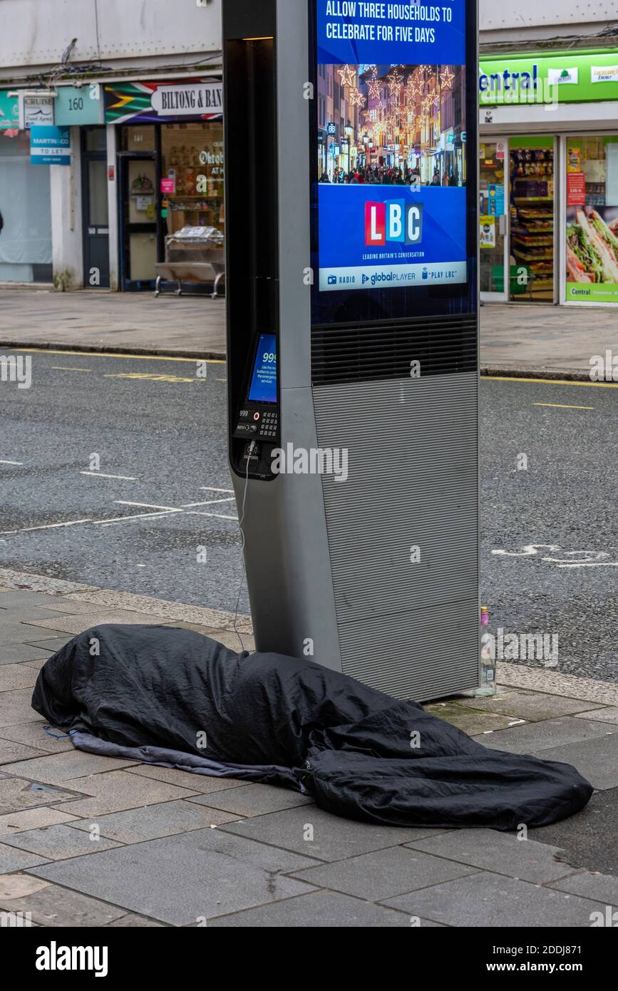 Personne sans-abri dormant difficilement à côté d'un appareil mobile ou d'un chargeur de téléphone en charge de téléphone mobile dans la rue. Banque D'Images