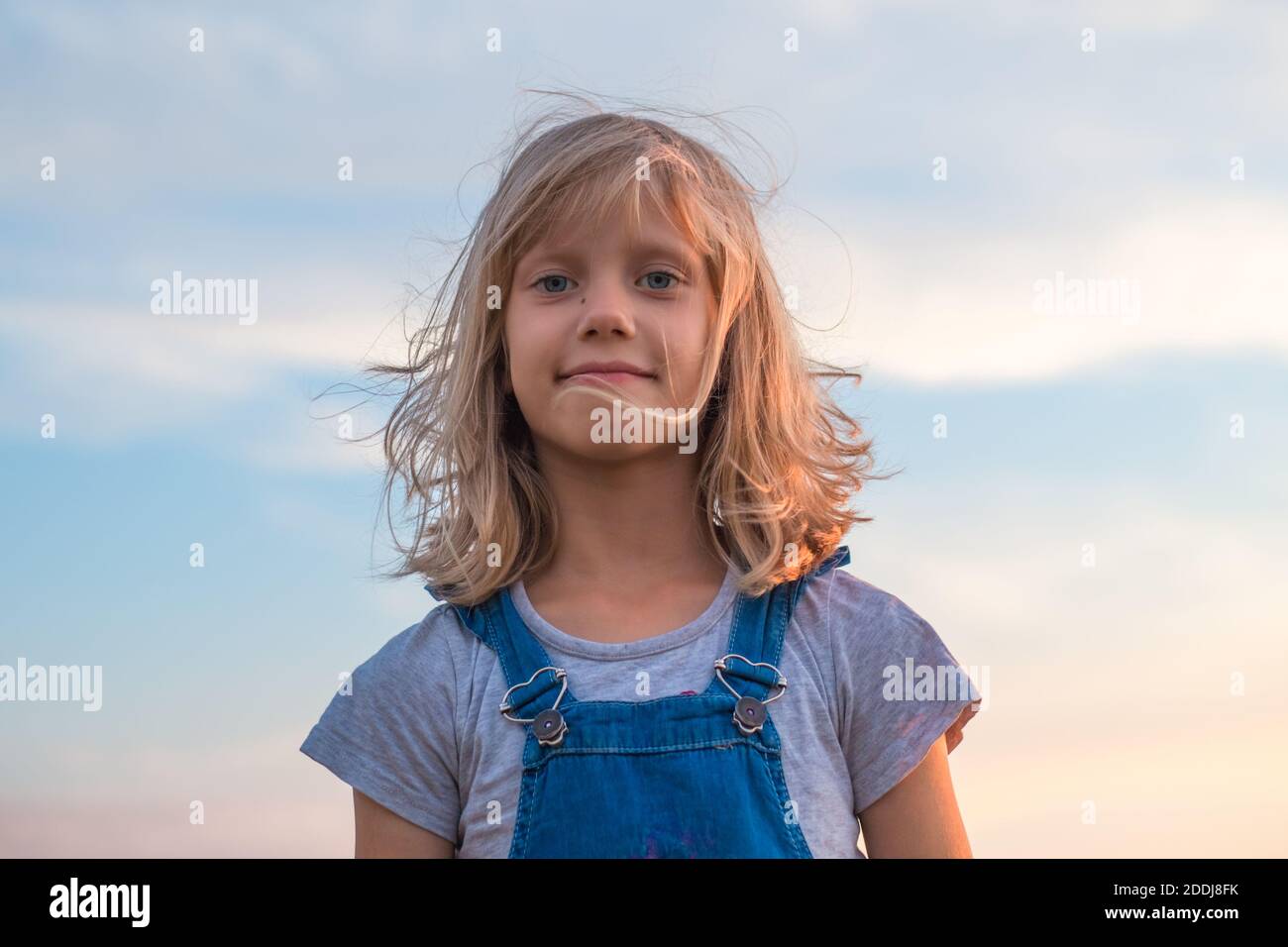 portrait d'une fille avec de grands yeux et des cheveux blonds en développement contre le ciel. Banque D'Images