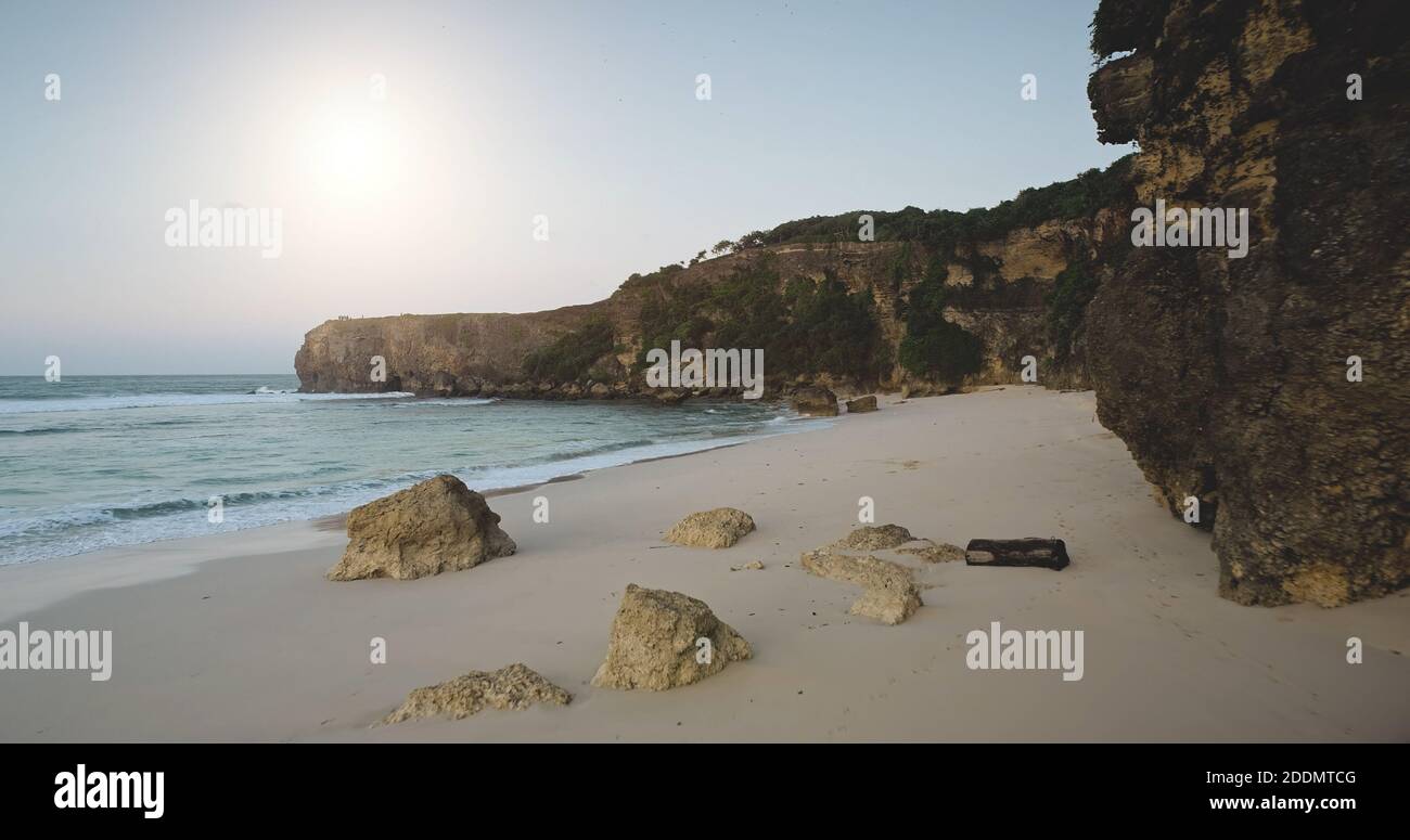 Plage de sable clair au soleil avec vue aérienne sur les vagues de l'océan. L'eau au bord de la mer sablonneuse avec falaise et pierres. Magnifique île de Sumba, paysage marin de l'Indonésie à la journée ensoleillée d'été. Tournage de drone de paysages cinématographiques Banque D'Images
