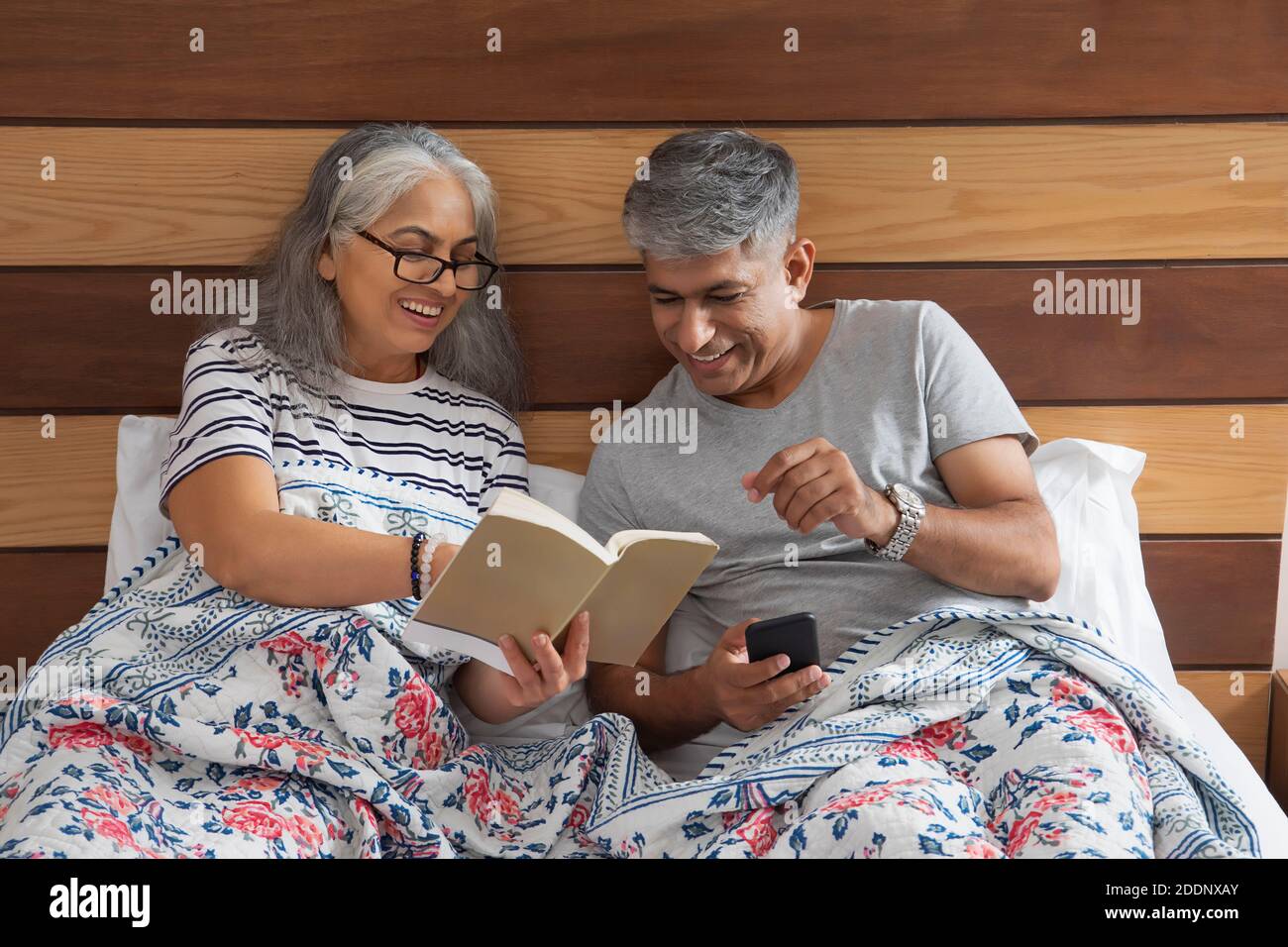 couple âgé assis au lit pour lire et échanger des notes Banque D'Images