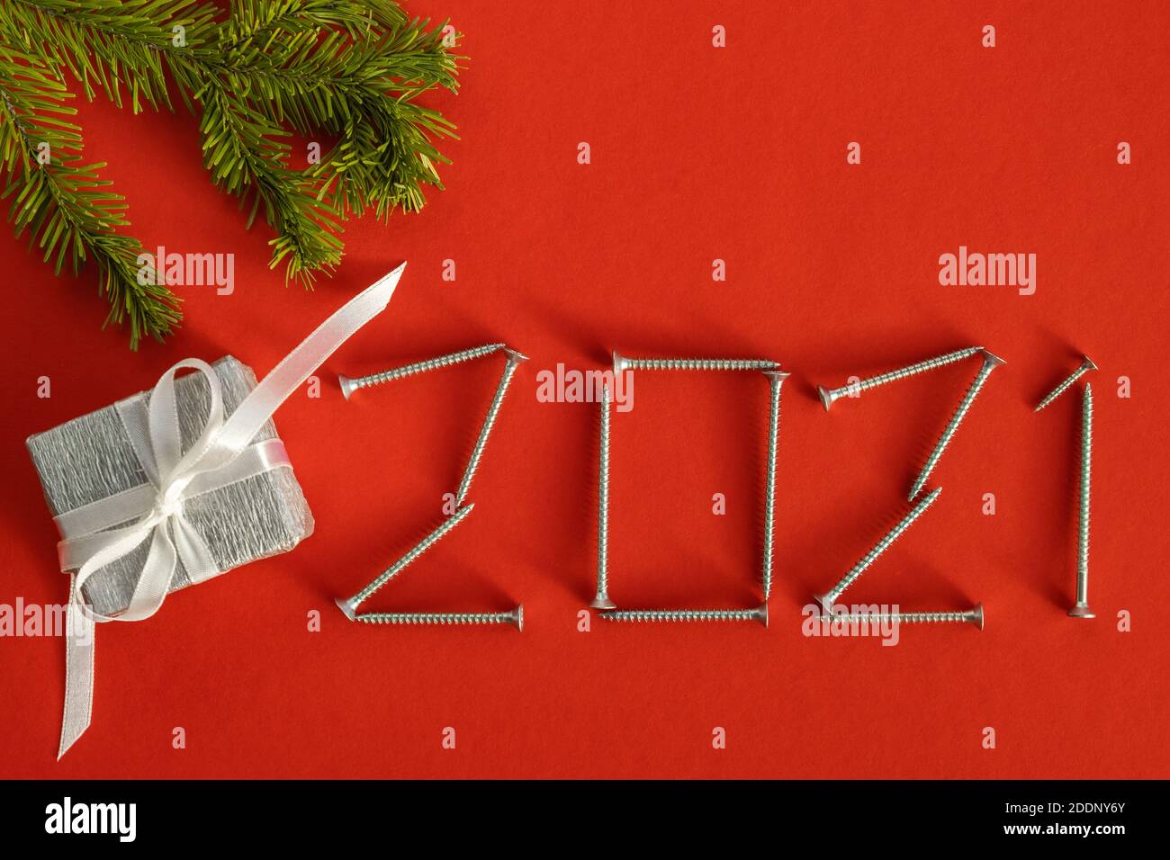 Carte de Noël créative. Numéro 2021 fait de vis sur fond rouge avec cadeau et une branche d'épinette. Concept créatif de la nouvelle année. Copier l'espace. Banque D'Images