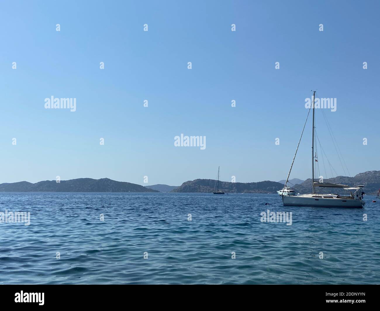 Voile sur les eaux bleu turquoise de la mer Égée. Yacht blanc dans la baie et les îles à l'horizon. Ciel bleu clair. Banque D'Images