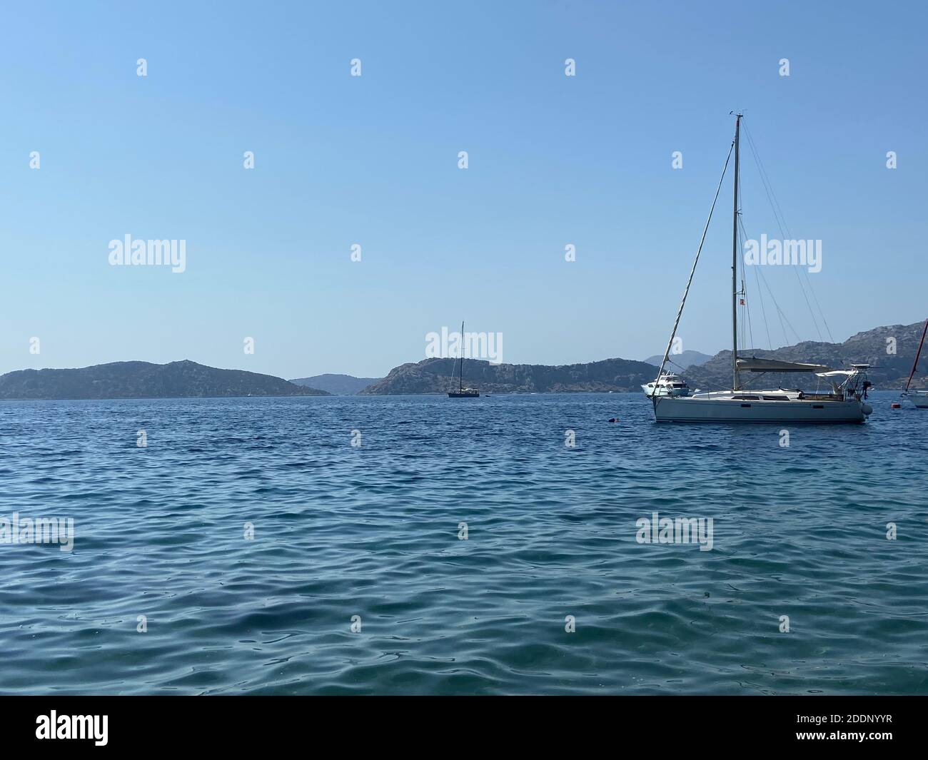 Voile sur les eaux bleu turquoise de la mer Égée. Yacht blanc dans la baie et les îles à l'horizon. Ciel bleu clair. Banque D'Images