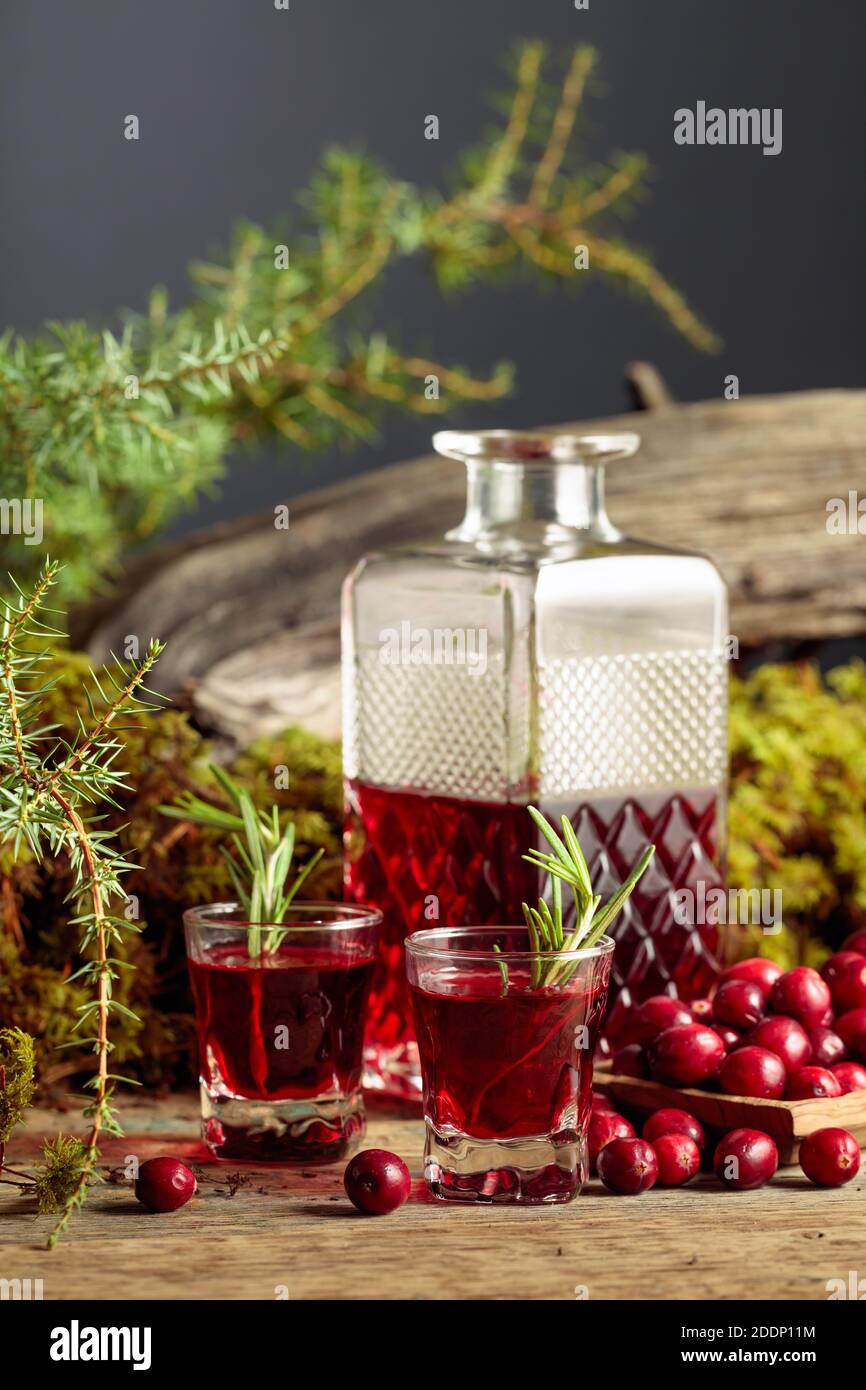 Canneberges et liqueur de canneberges sur une vieille table en bois. Dans la mousse d'arrière-plan, branche de genévrier, et le vieux museau. Banque D'Images