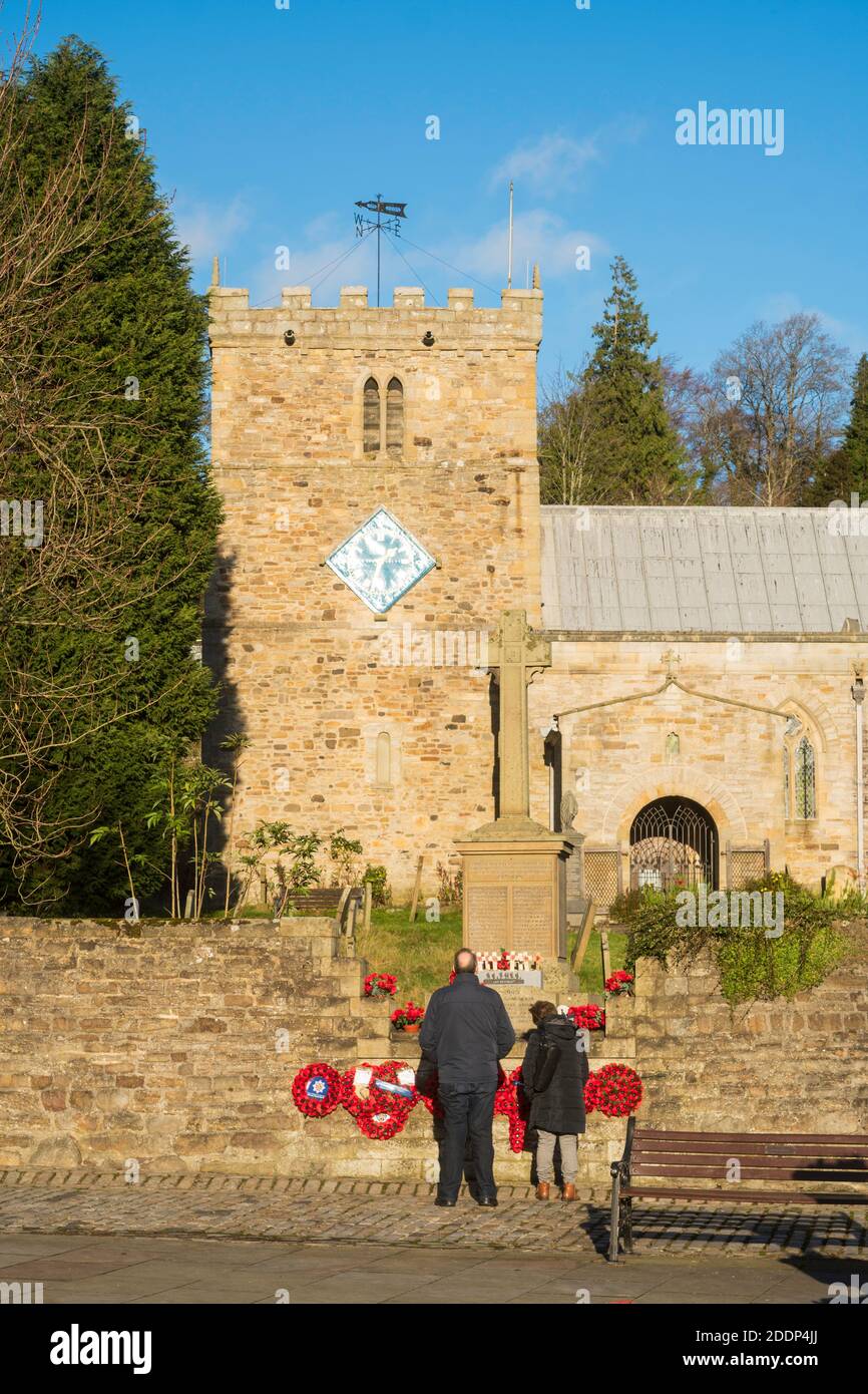 Couple plus âgé inspectant le mémorial de guerre et l'église de Saint Thomas l'Apôtre à Stanhope, Co. Durham, Angleterre, Royaume-Uni Banque D'Images