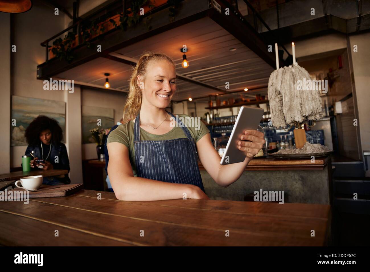 Femme souriante qui se tient debout sur une table à l'aide d'une tablette numérique dans un café moderne Banque D'Images