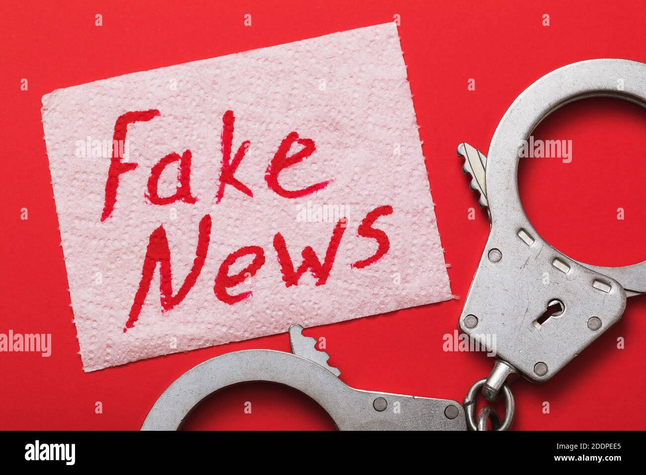 Menottes et une feuille de papier toilette avec inscription sur fond rouge. Concept de punition des fausses nouvelles Banque D'Images