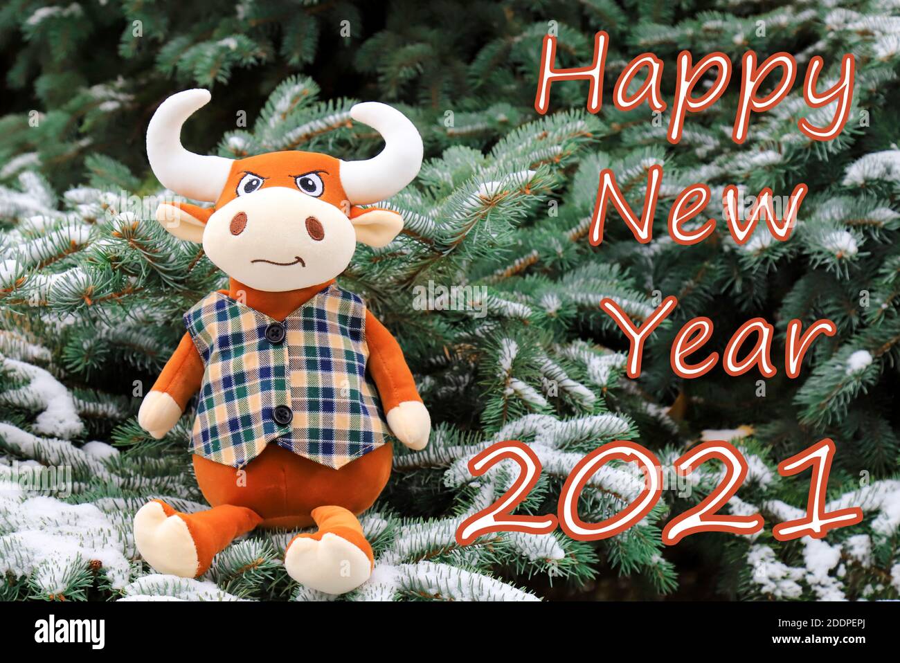 Carte de Noël avec inscription - bonne année 2021. Un drôle de jouet orange Bull se trouve sur un arbre de Noël recouvert de neige, symbole de la nouvelle année 2021 Banque D'Images