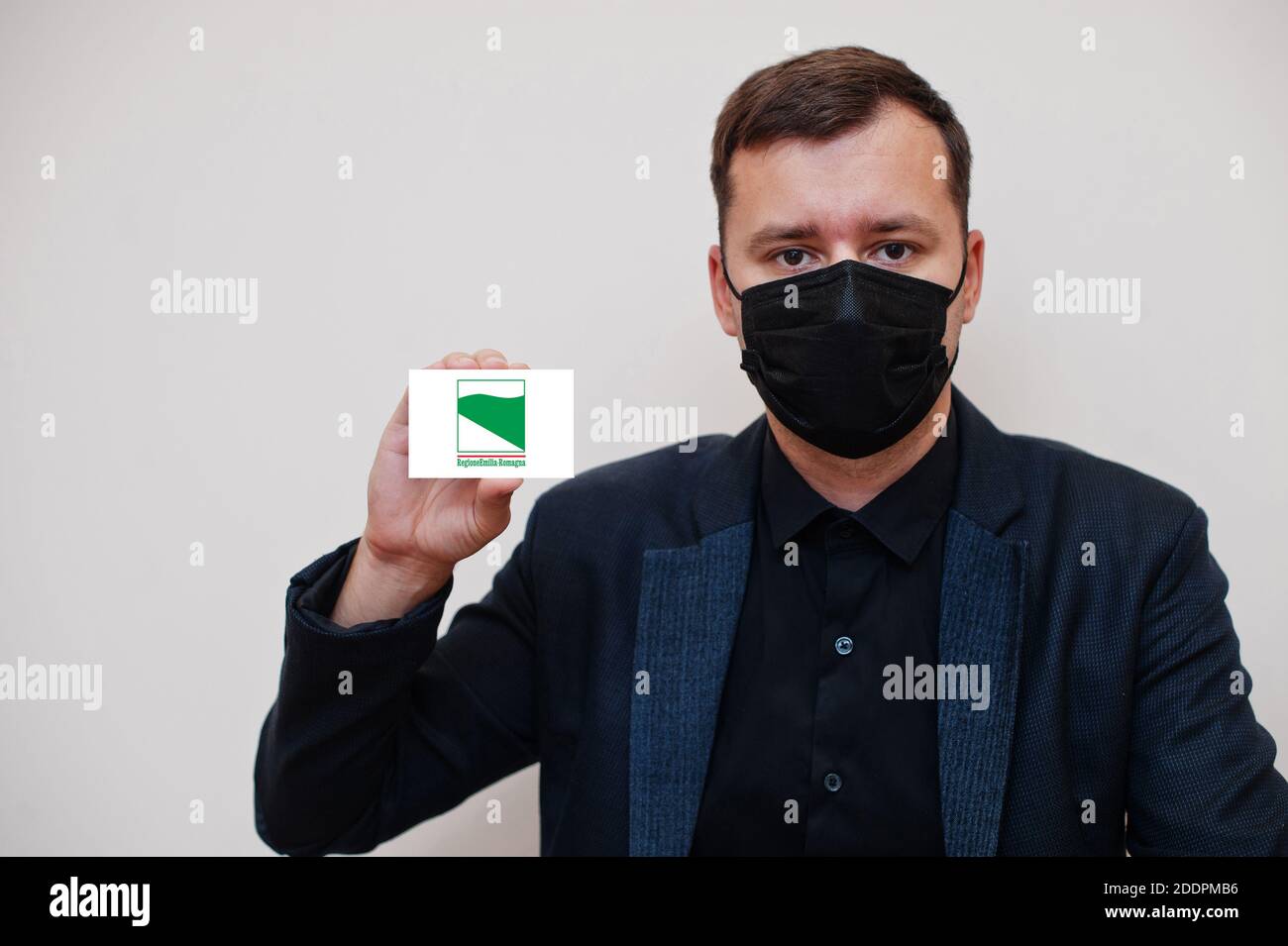 L'homme italien porte un masque classique noir et protège le visage, tient la carte drapeau Emilia-Romagna isolée sur fond blanc. Italie régions coronavirus Covid conce Banque D'Images