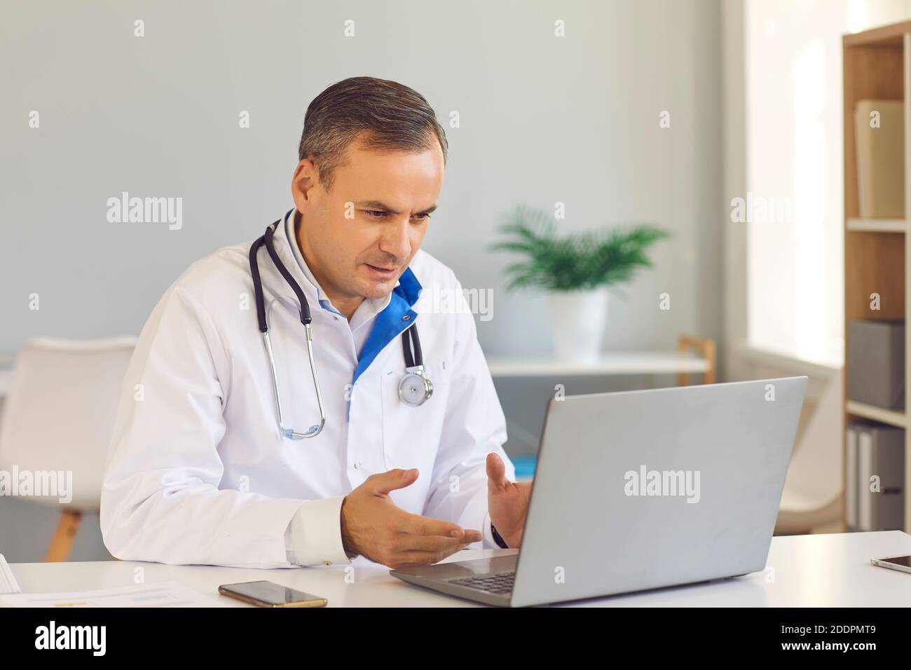 Médecin assis à l'ordinateur portable, appel vidéo du patient et consultation médicale en ligne Banque D'Images
