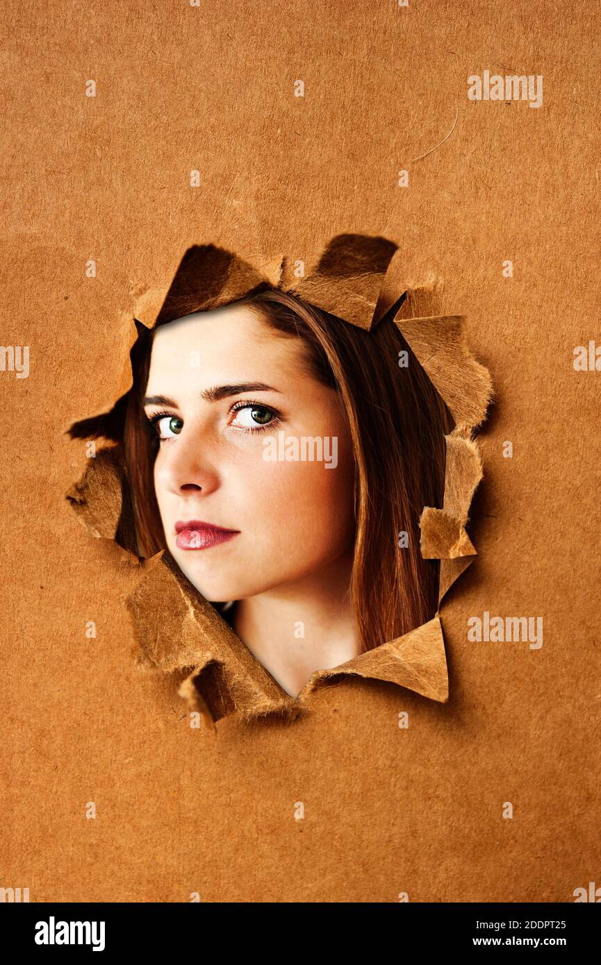 visage d'une adolescente regardant de derrière une rip sur fond papier Banque D'Images